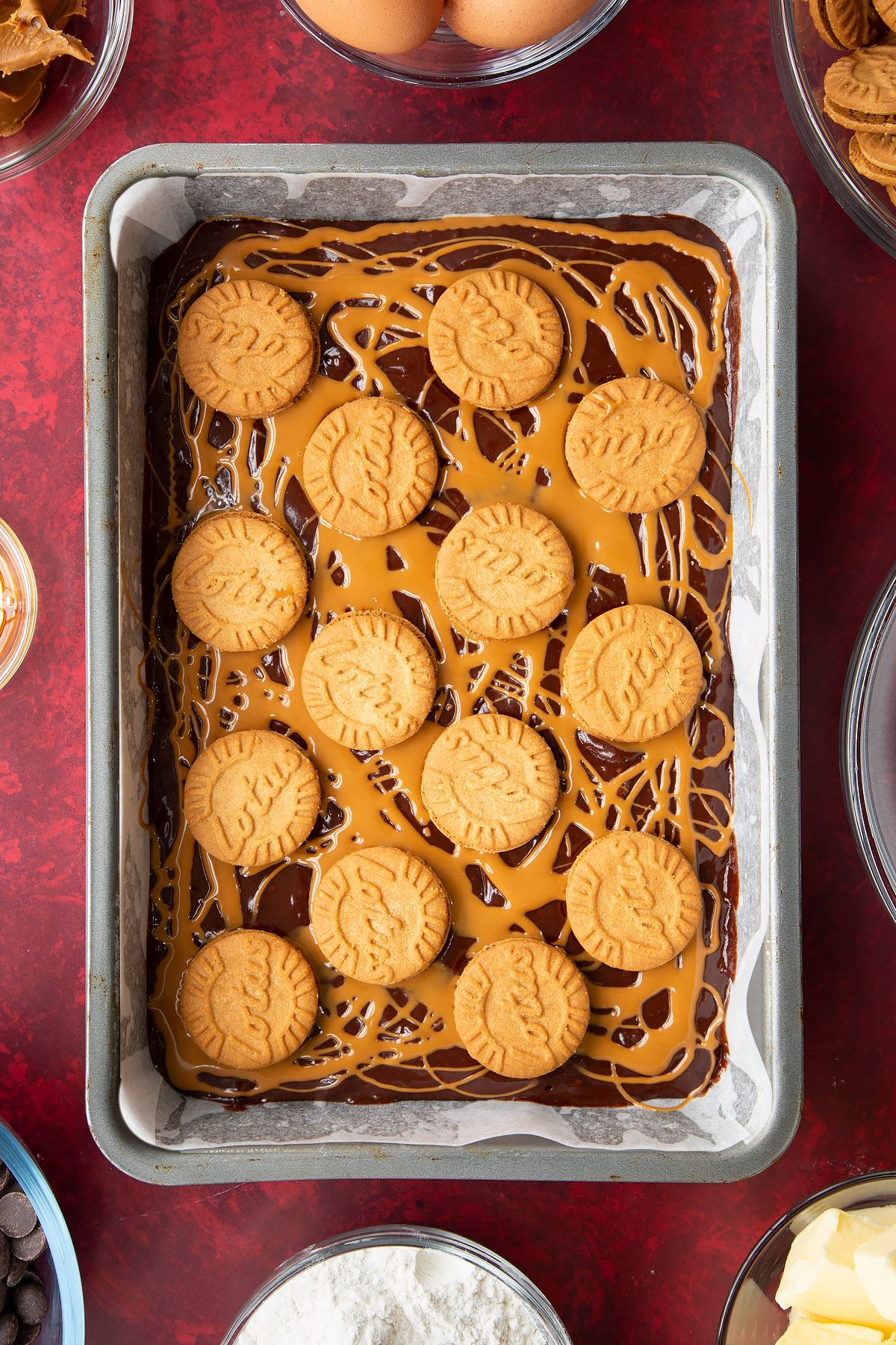 brownie batter in a lined baking tin drizzled with biscoff spread and topped with lotus biscoff biscuits.