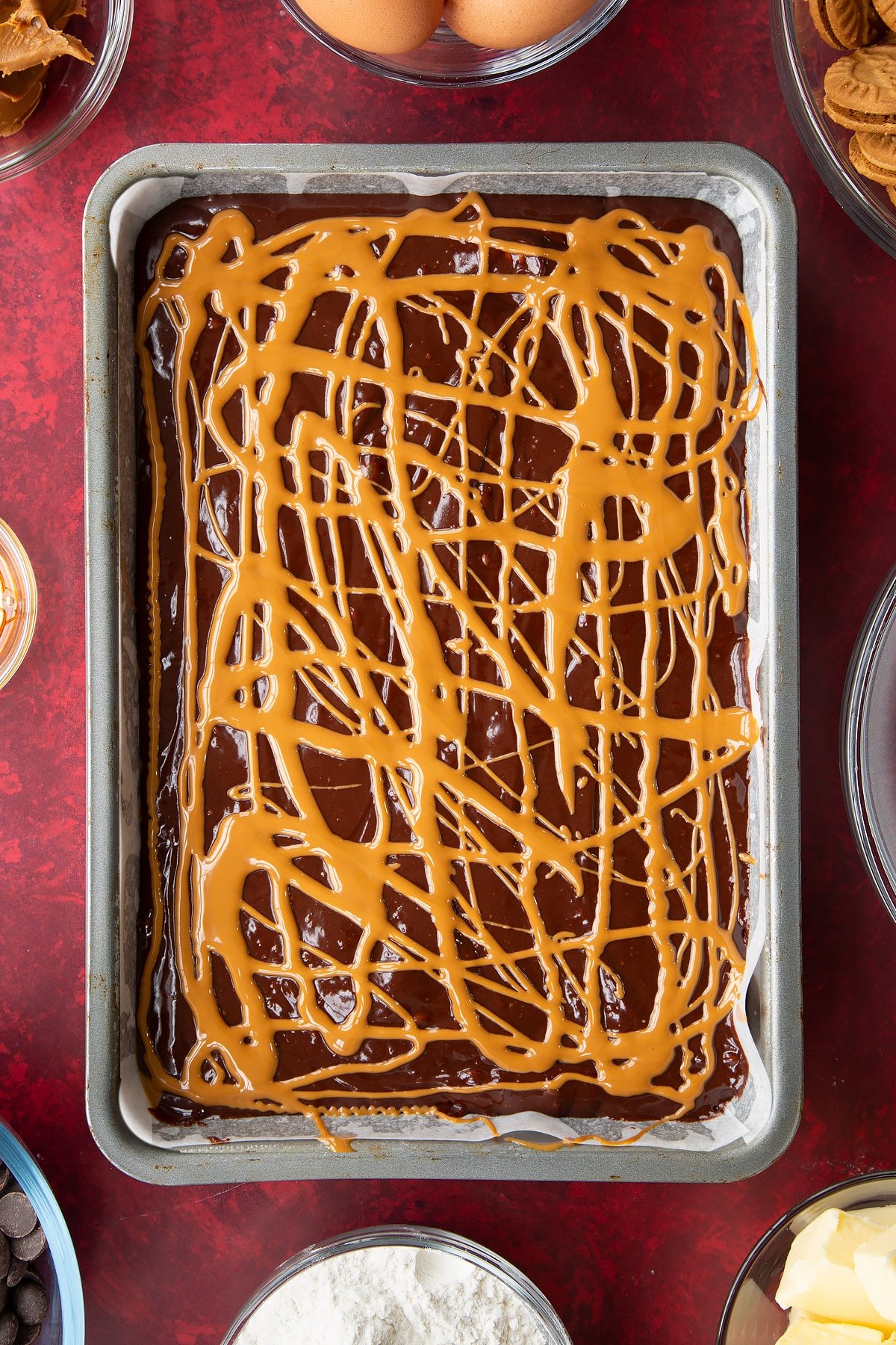 brownie batter in a large lined baking tin drizzled with biscoff spread.