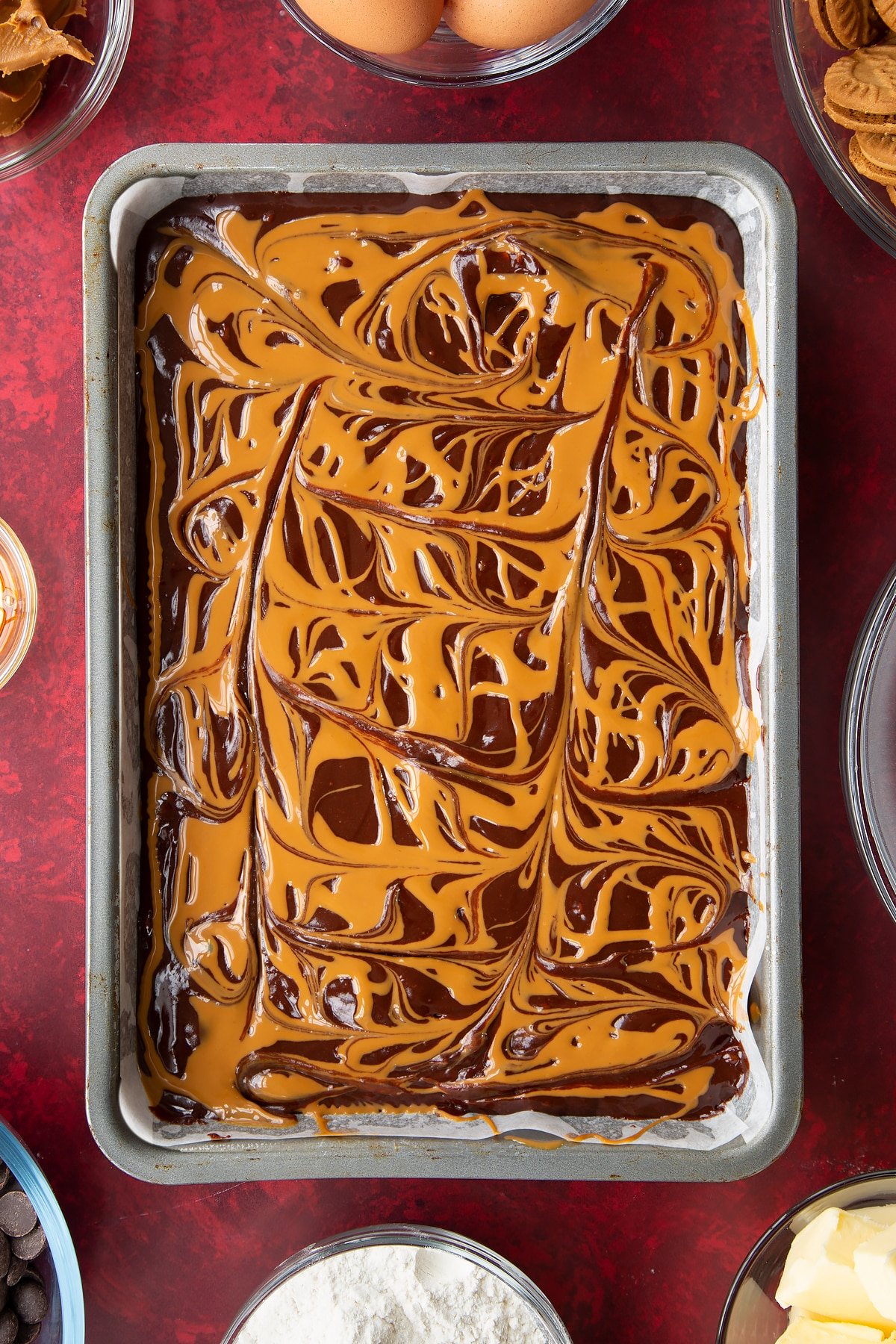 brownie batter in a large lined baking tin drizzled with biscoff spread.