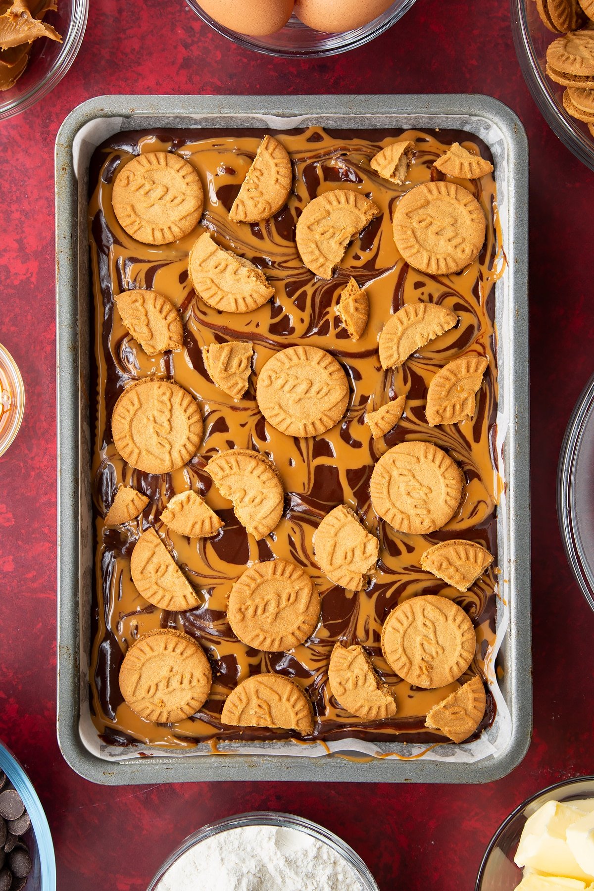 brownie batter in a large lined baking tin drizzled with biscoff spread topped with lotus biscuits.