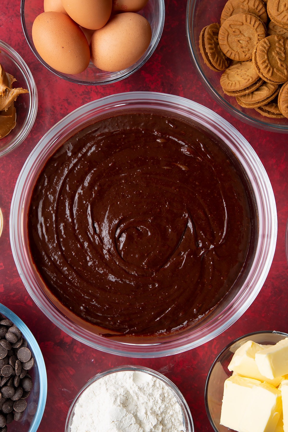 chocolate batter in a large clear bowl surrounded by ingredients.