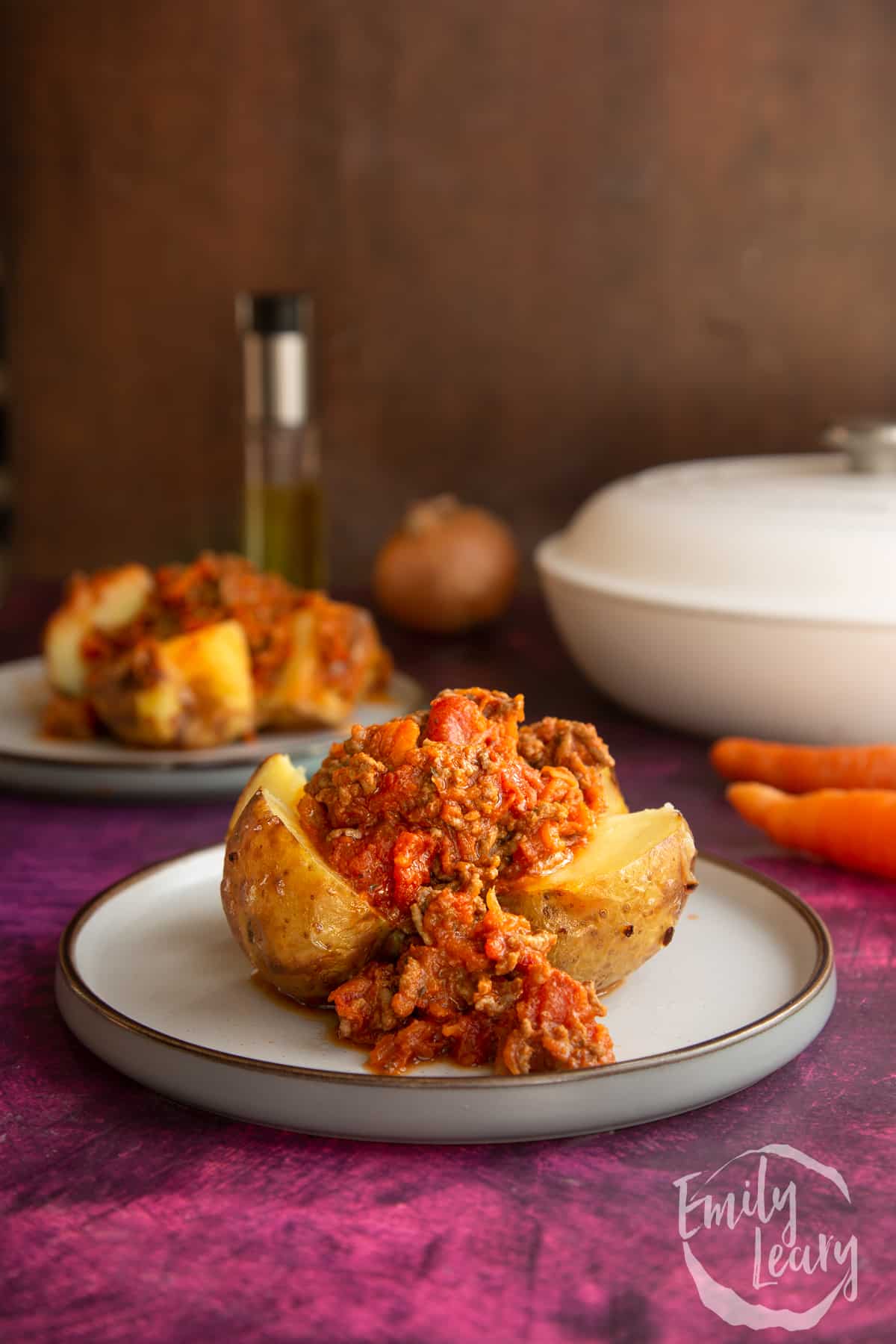 a cooked jacket potato cut in half topped with bolognese sauce on a white plate.
