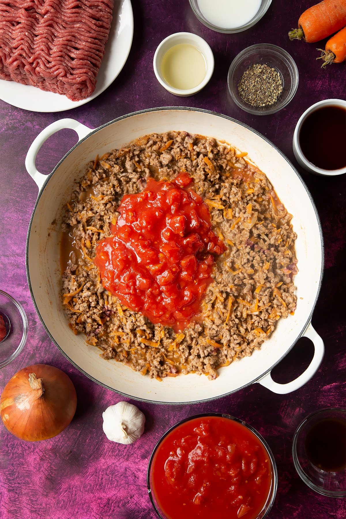 cooked bolognese sauce topped with tomatoes in a frying pan surrounded by ingredients.