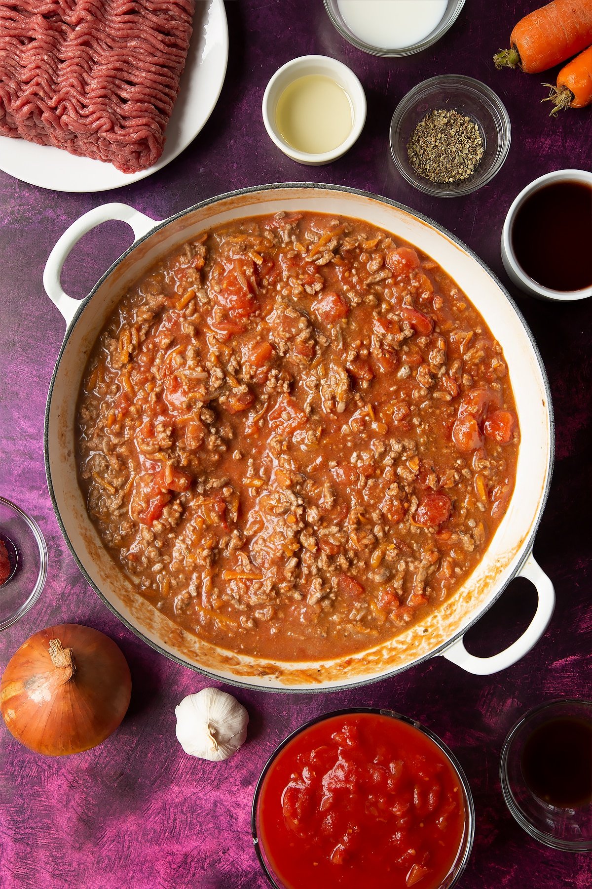 cooked bolognese sauce in a frying pan surrounded by ingredients.