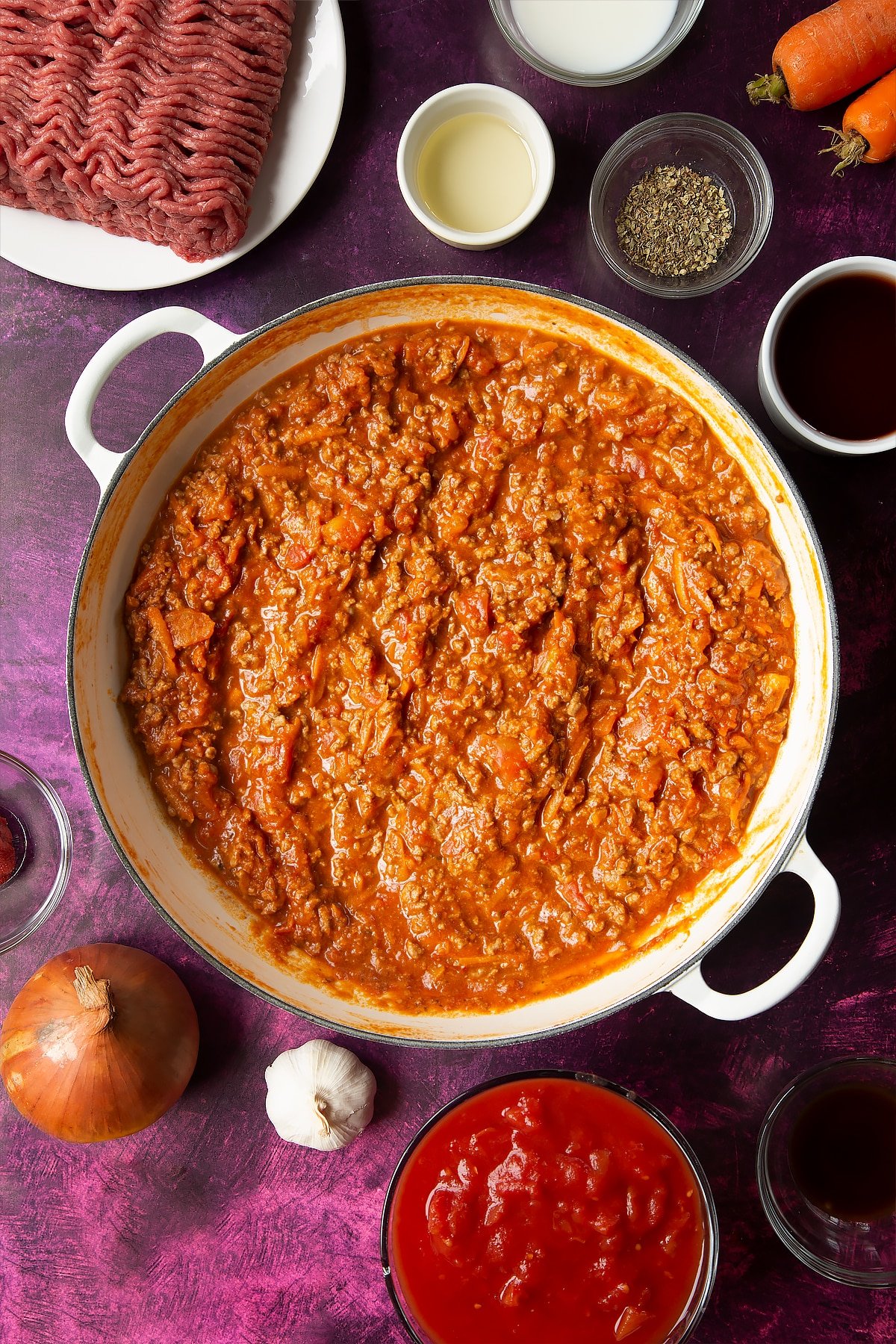 cooked bolognese sauce in a frying pan surrounded by ingredients.
