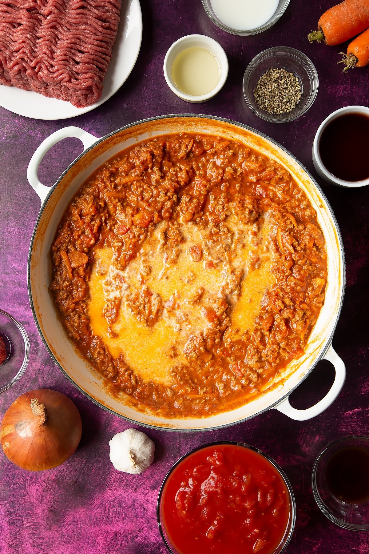 cooked bolognese sauce in a frying pan topped with milk surrounded by ingredients
