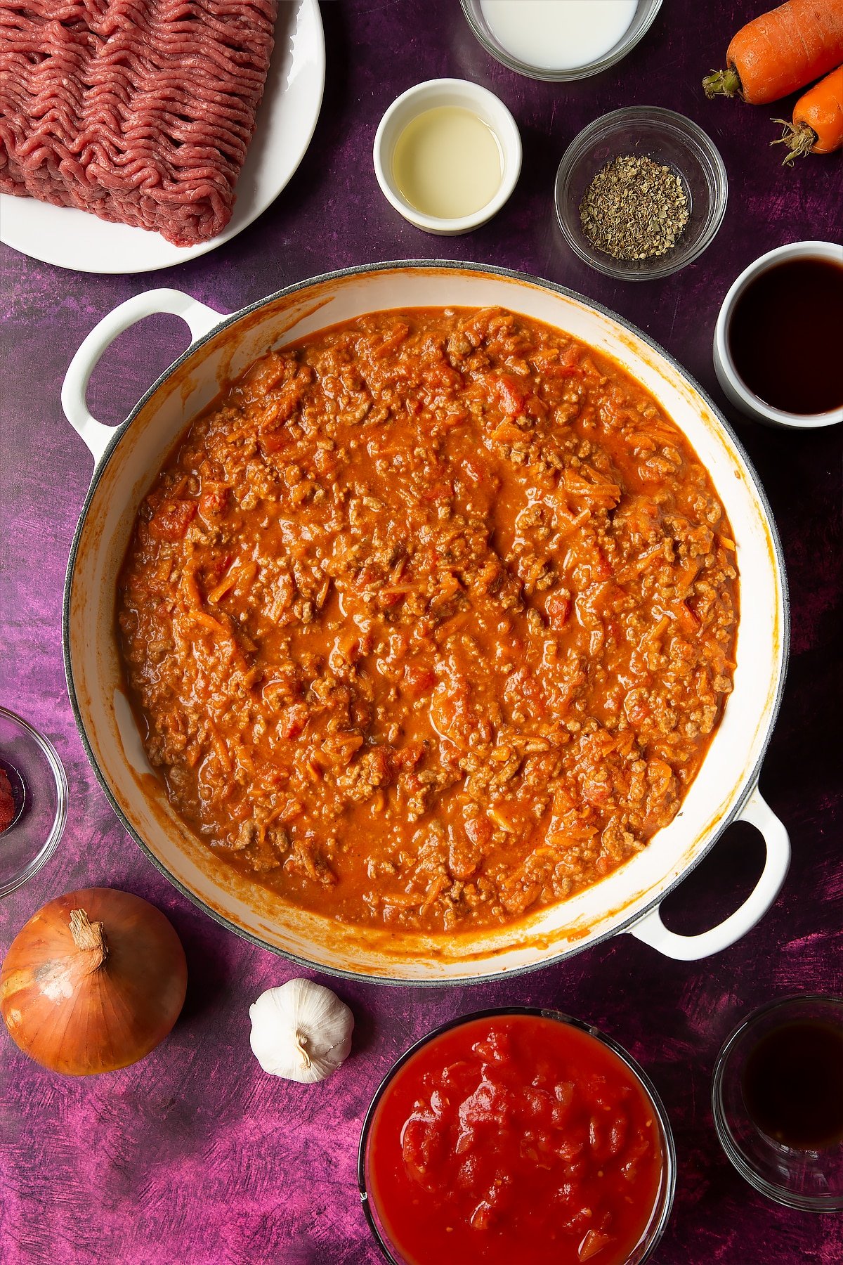 an overhead view of a large casserole dish with bolognese sauce surrounded by ingredients.