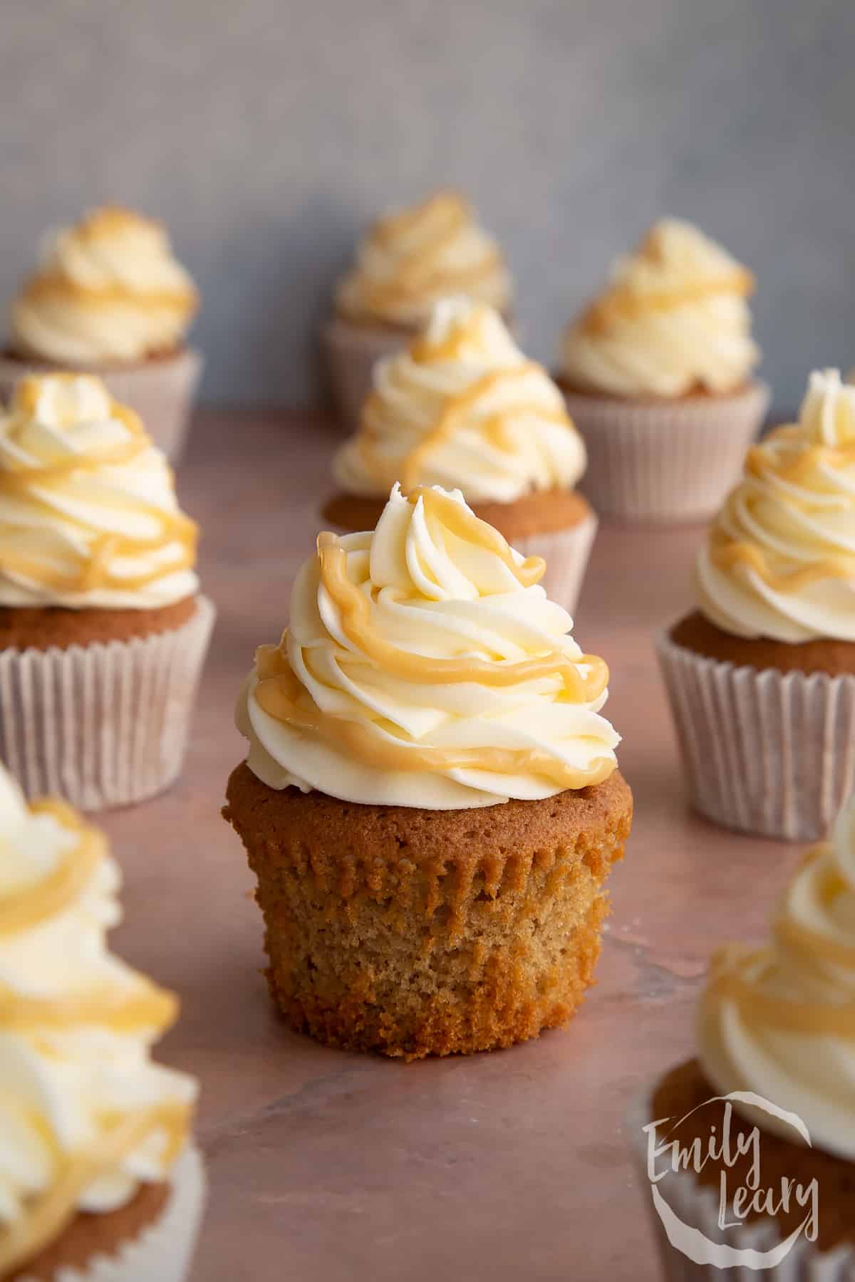 caramel latte cupcake sat in the centre of more cupckes in white cupcake liners.