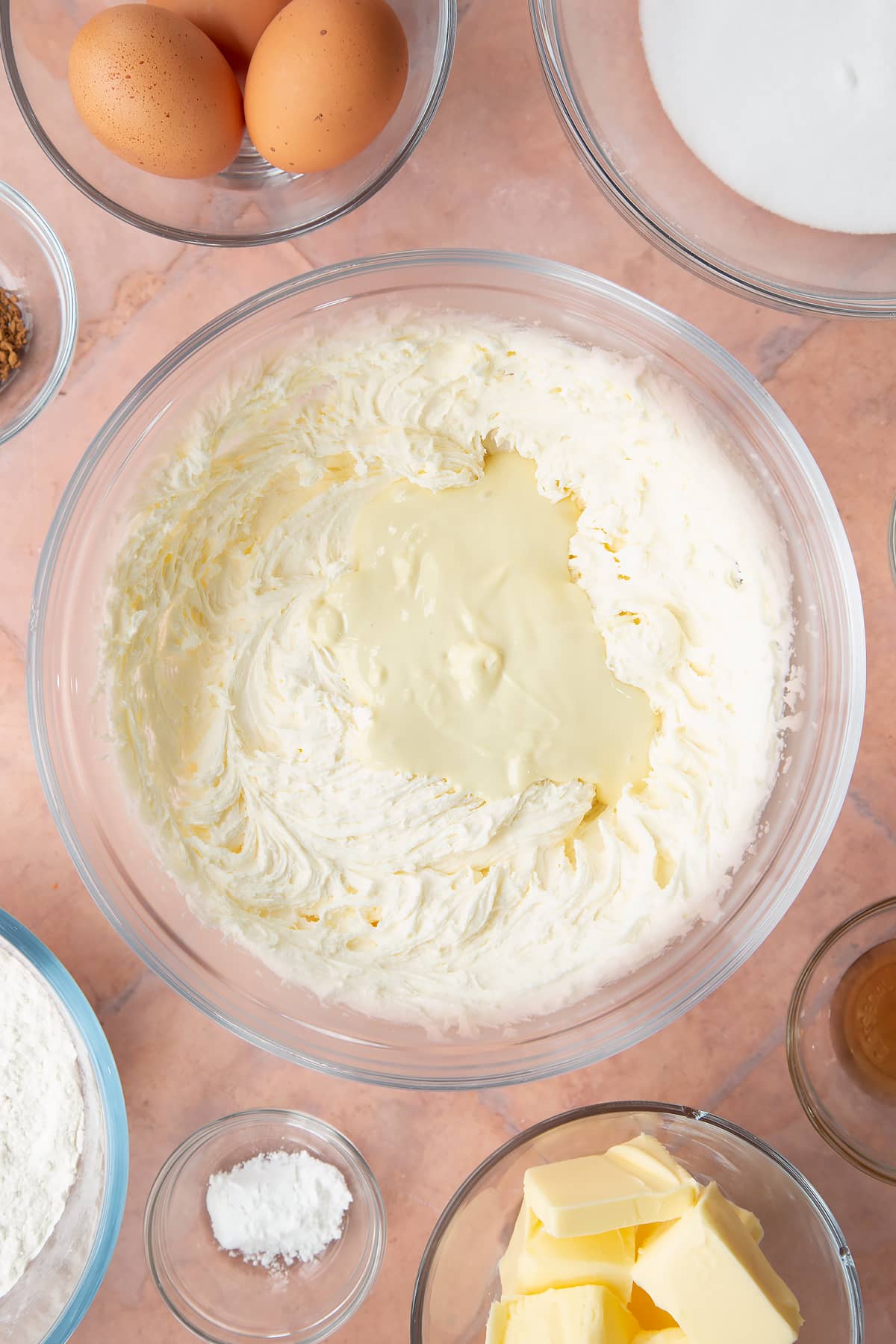 whisked buttercream icing in a large clear bowl topped with melted white chocolate.