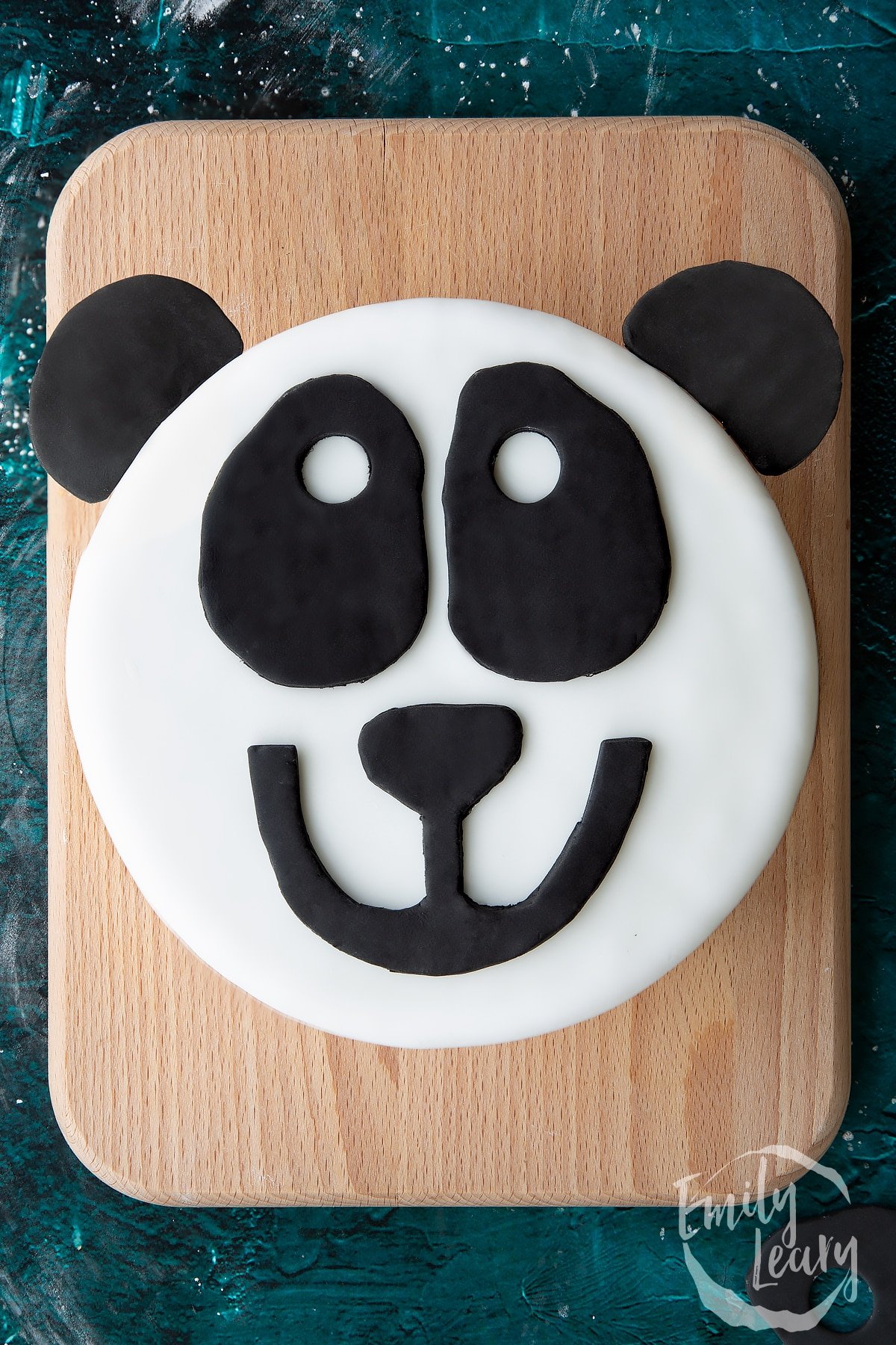 a panda face made of icing on a cake on a wooden board.