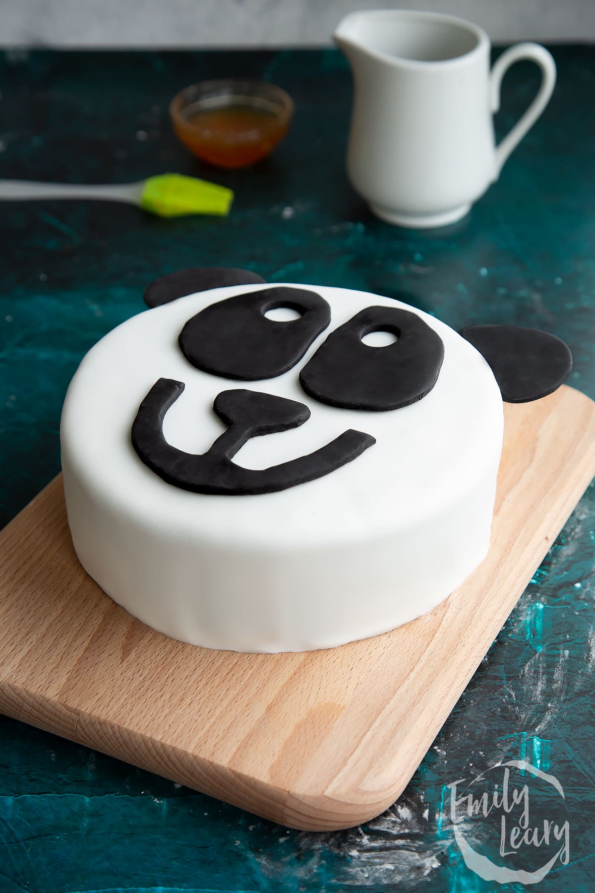 a cute animated panda face made of icing on a cake on w wooden baord.