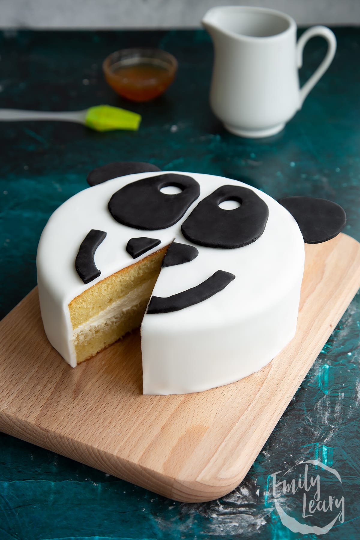 a panda face cake with ears on the top on a wooden board with a slice cut out the front.
