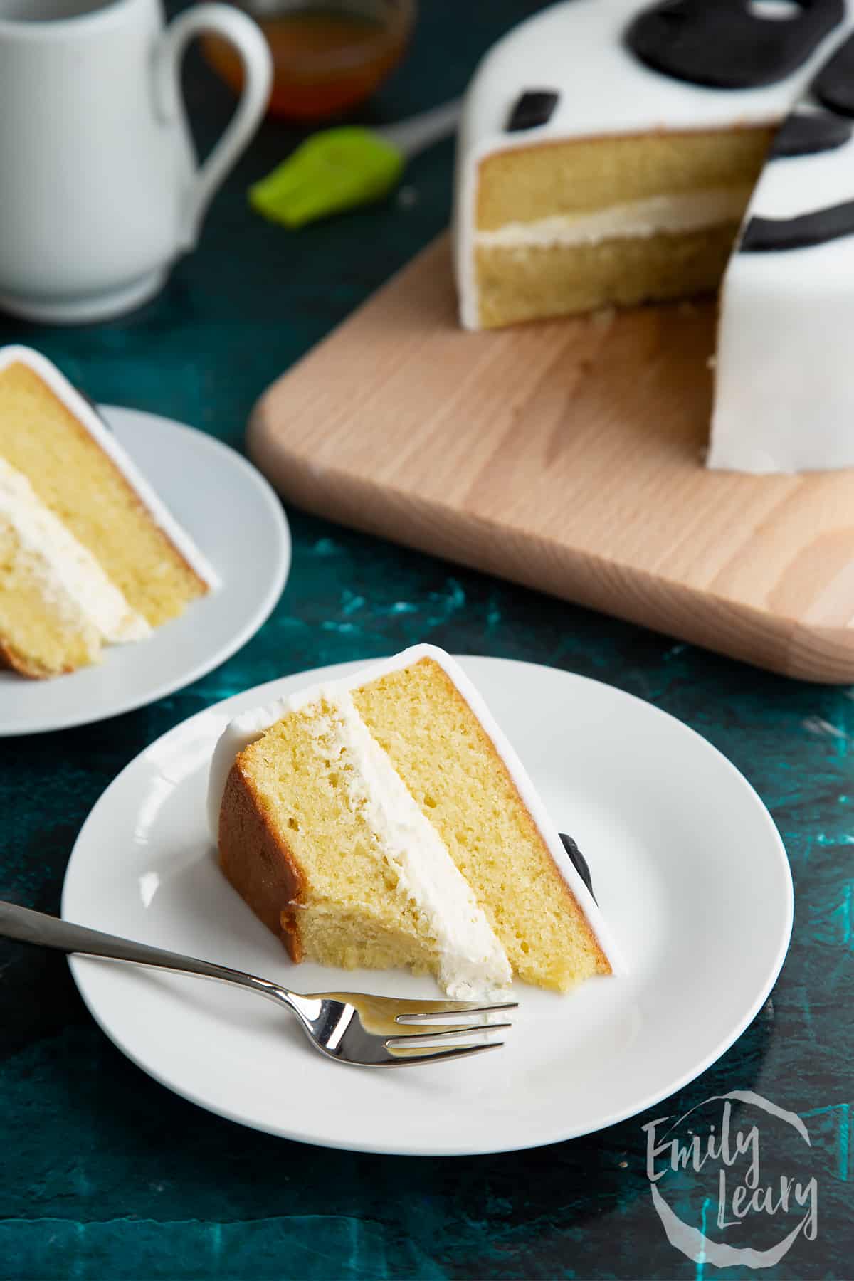 a slice of vanilla cake with buttercream icing on a white plate with a fork cutting off the front.