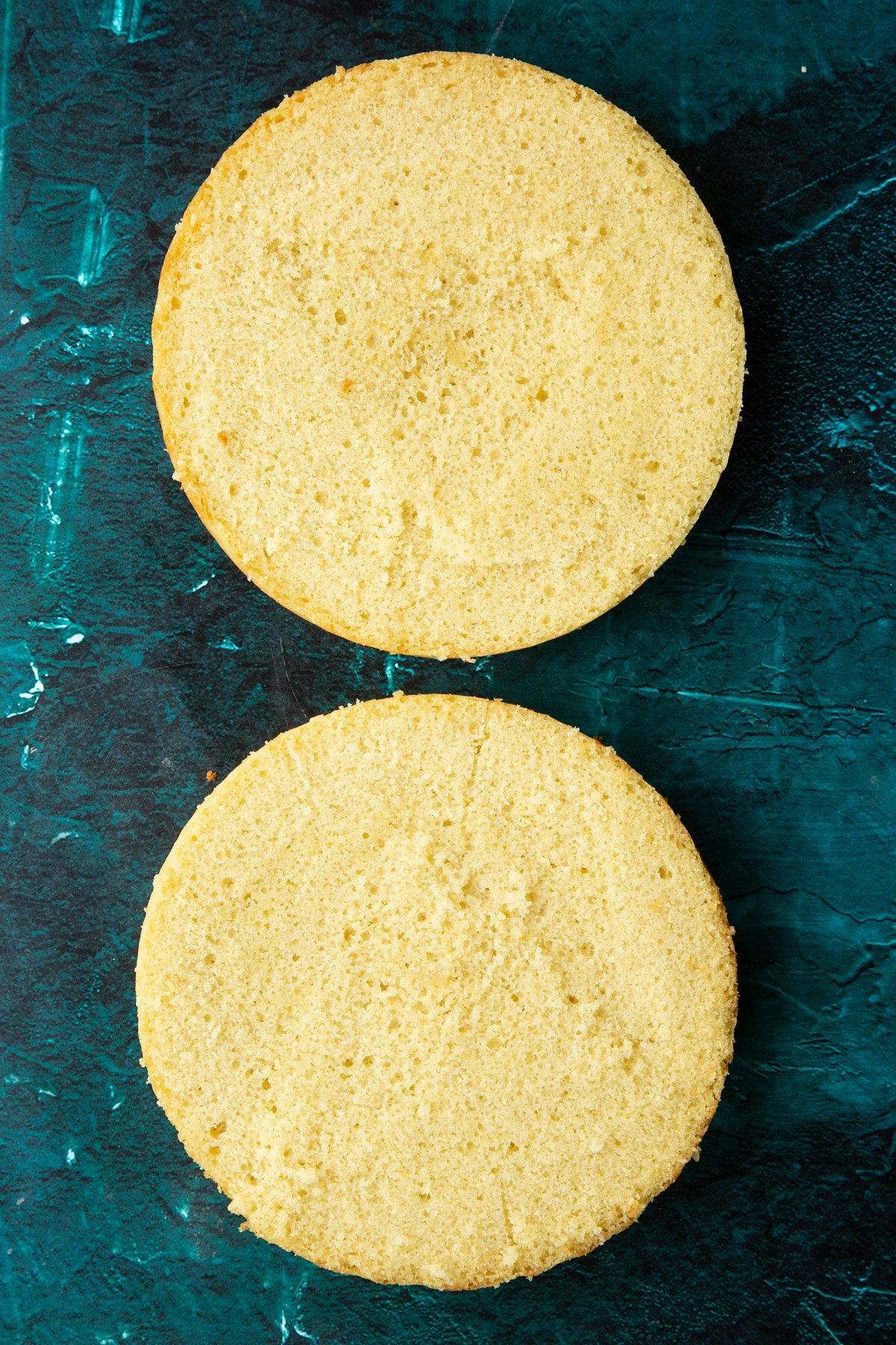 vanilla sponge cake cut in half on a green marble background.