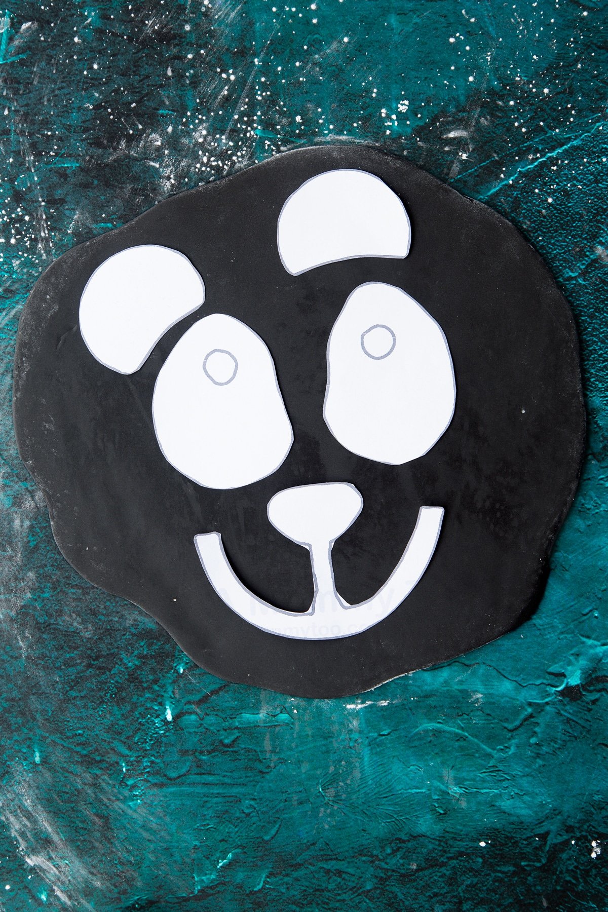 paper cut outs of a panda face placed on black royal icing.