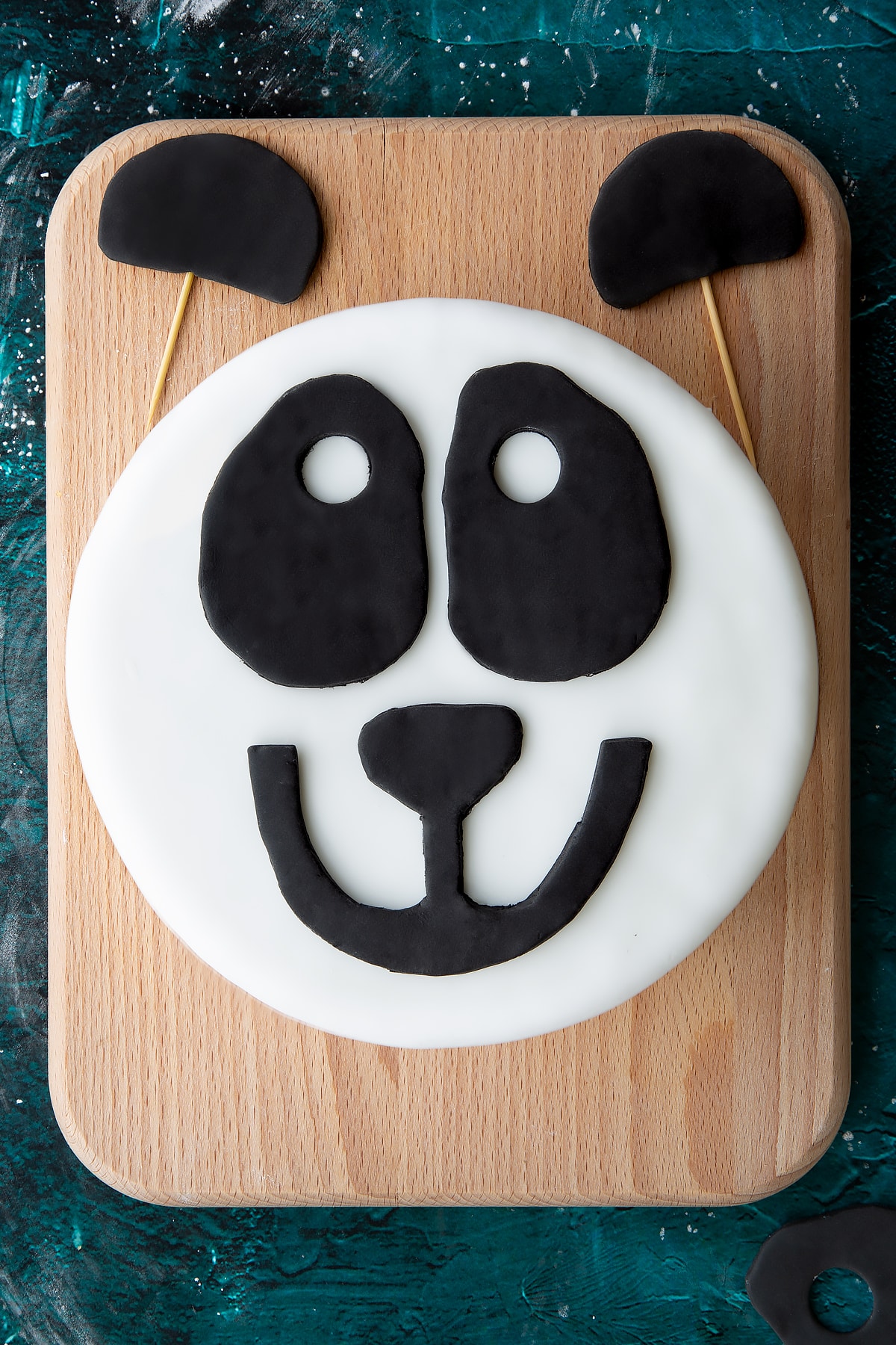 black royal icing panda features on a white royal icing covered cake on a green marble background with two black ears at the top.