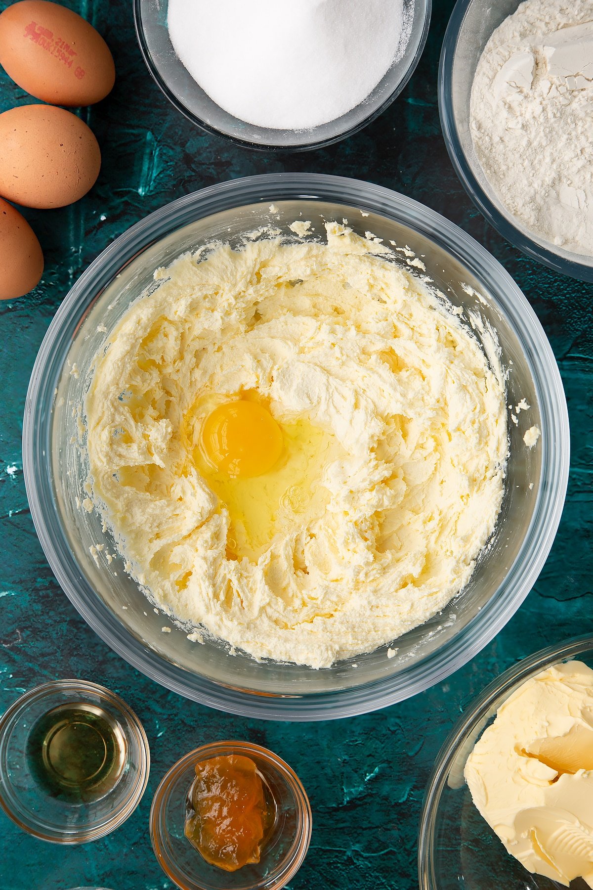 creamed sugar and margarine in a large mixing bowl topped with an egg with ingredients in the background.