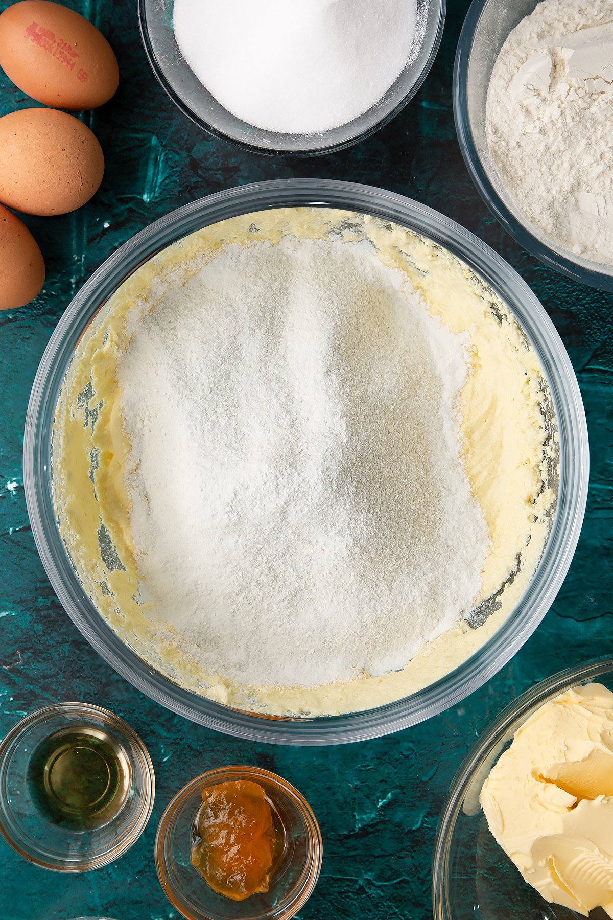 whisked cake batter in a large clear bowl topped with sifted flour.