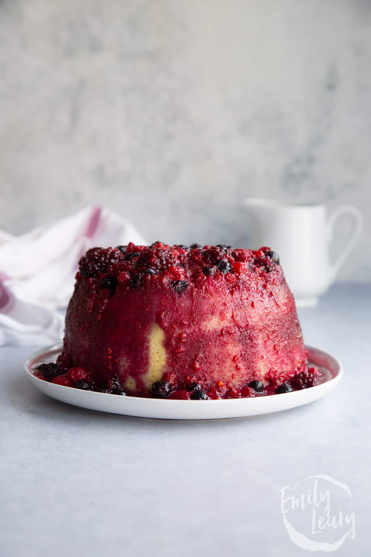 cooked summer fruit pudding on a white plare in a plain background.