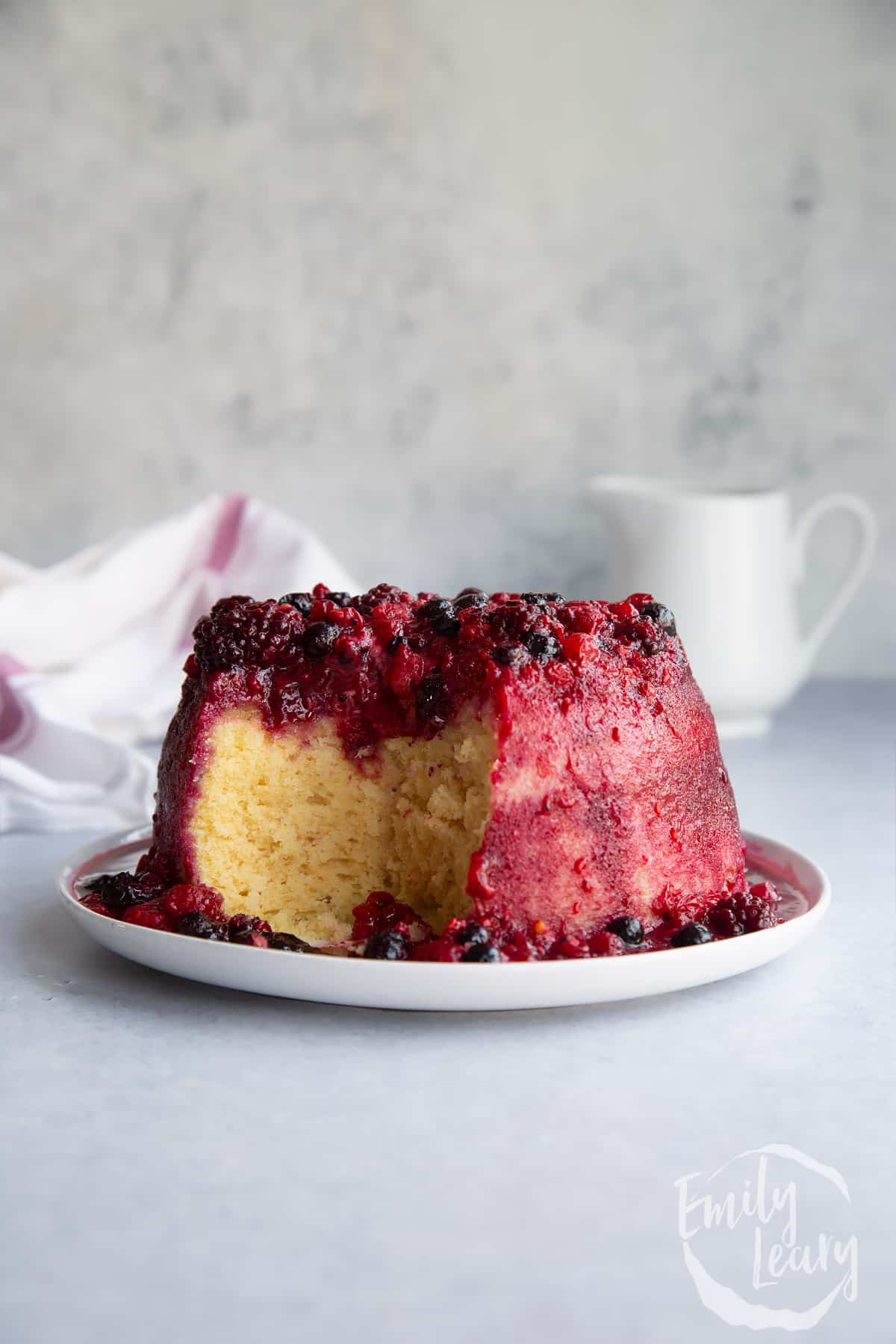 Summer fruit sponge pudding on a white plate with a piece cut from the middle.