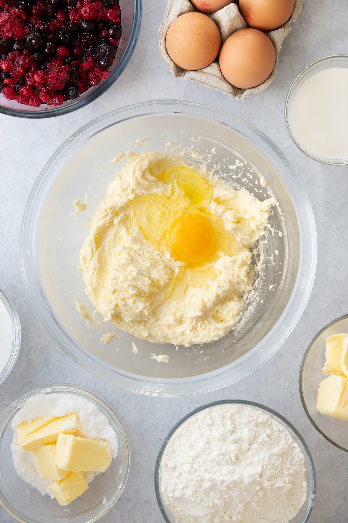 whisked sugar and butter in a large clear bowl surrounded by ingredients topped with one egg.