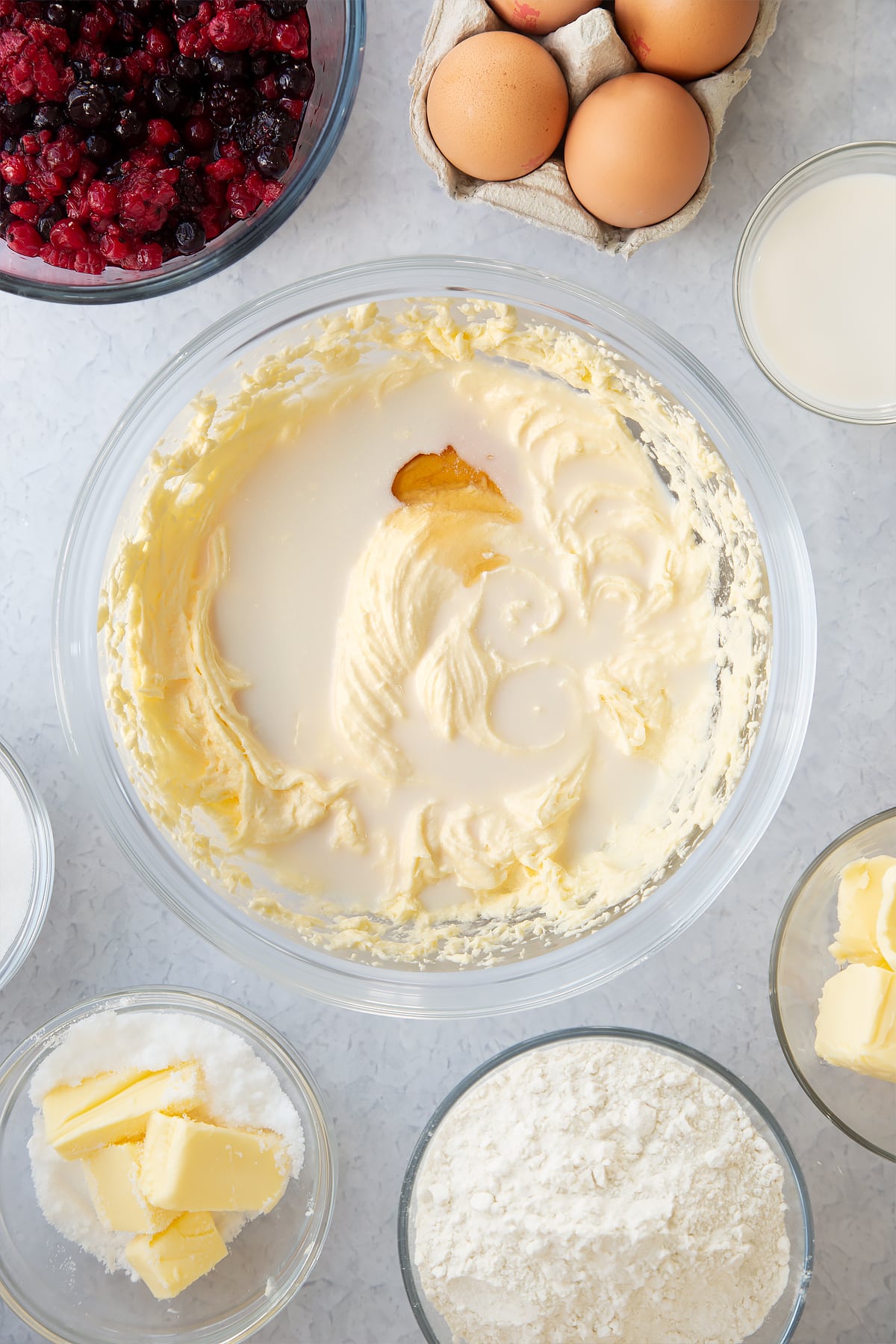 whisked cake batter mix in a large clear bowl topped with milk and vanilla essence.