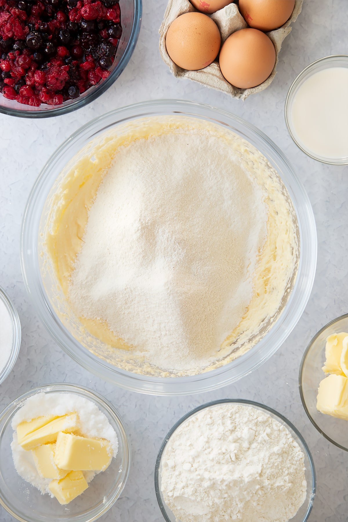 whisked cake batter mix in a large clear bowl topped with sifted flour.