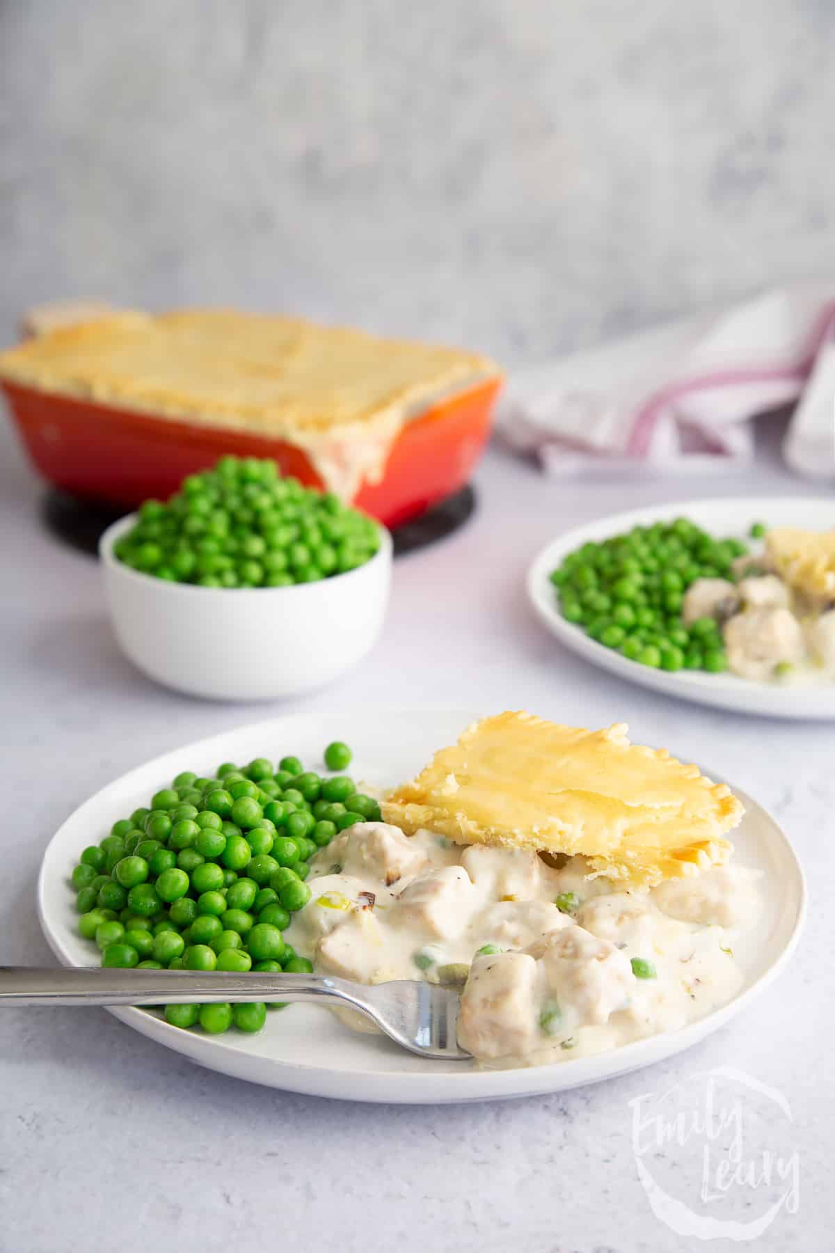 a piece of Gluten free vegetarian pie on a white plate with garden peas on the side and a fork at the front.
