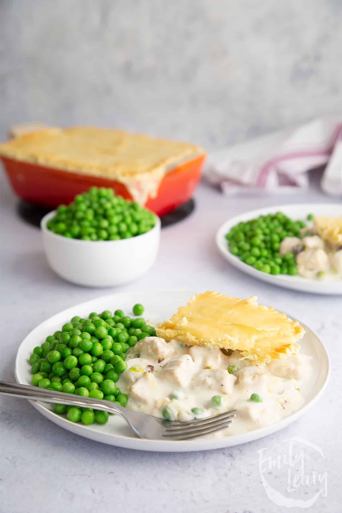 a piece of gluten free vegetarian pie on a white plate with peas and a fork on the side.