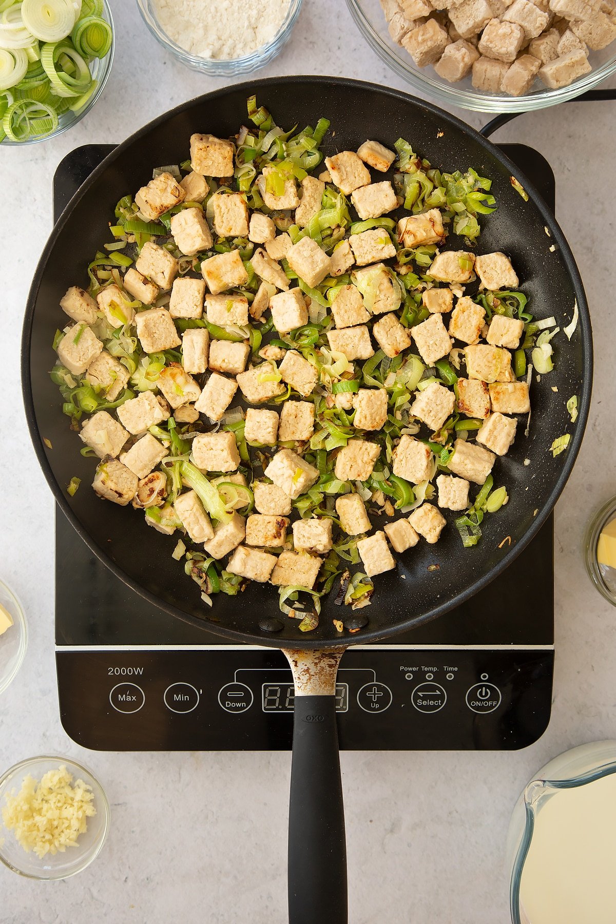 cooked leeks and vegetarian style chicken pieces in a large frying pan on an induction hob. 