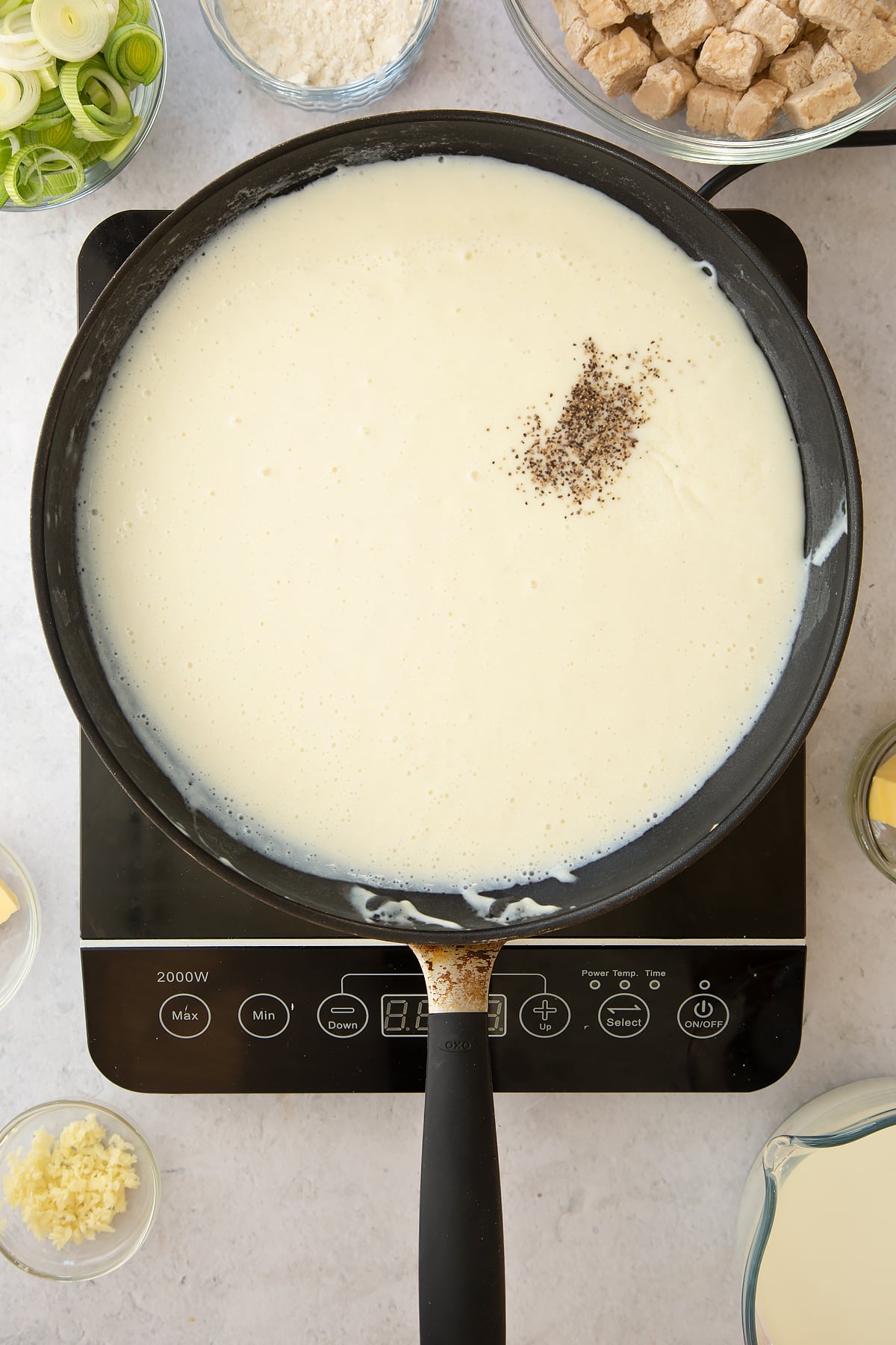 cooked milk and flour mix topped with a dash of pepper in a large frying pan on an induction hob.