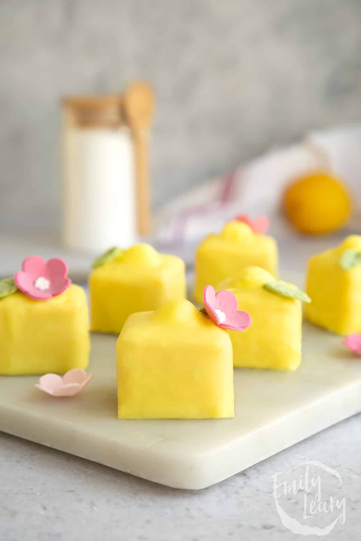 A number of lemon fondant fancies on a marble board.