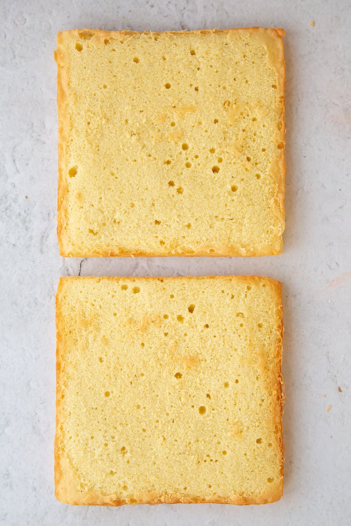 Two square sponge cakes on a marble board.