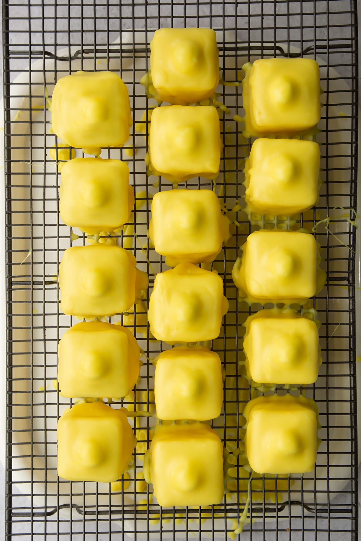 Drizzling the icing over the top of the lemon fondant fancies on a wire rack.