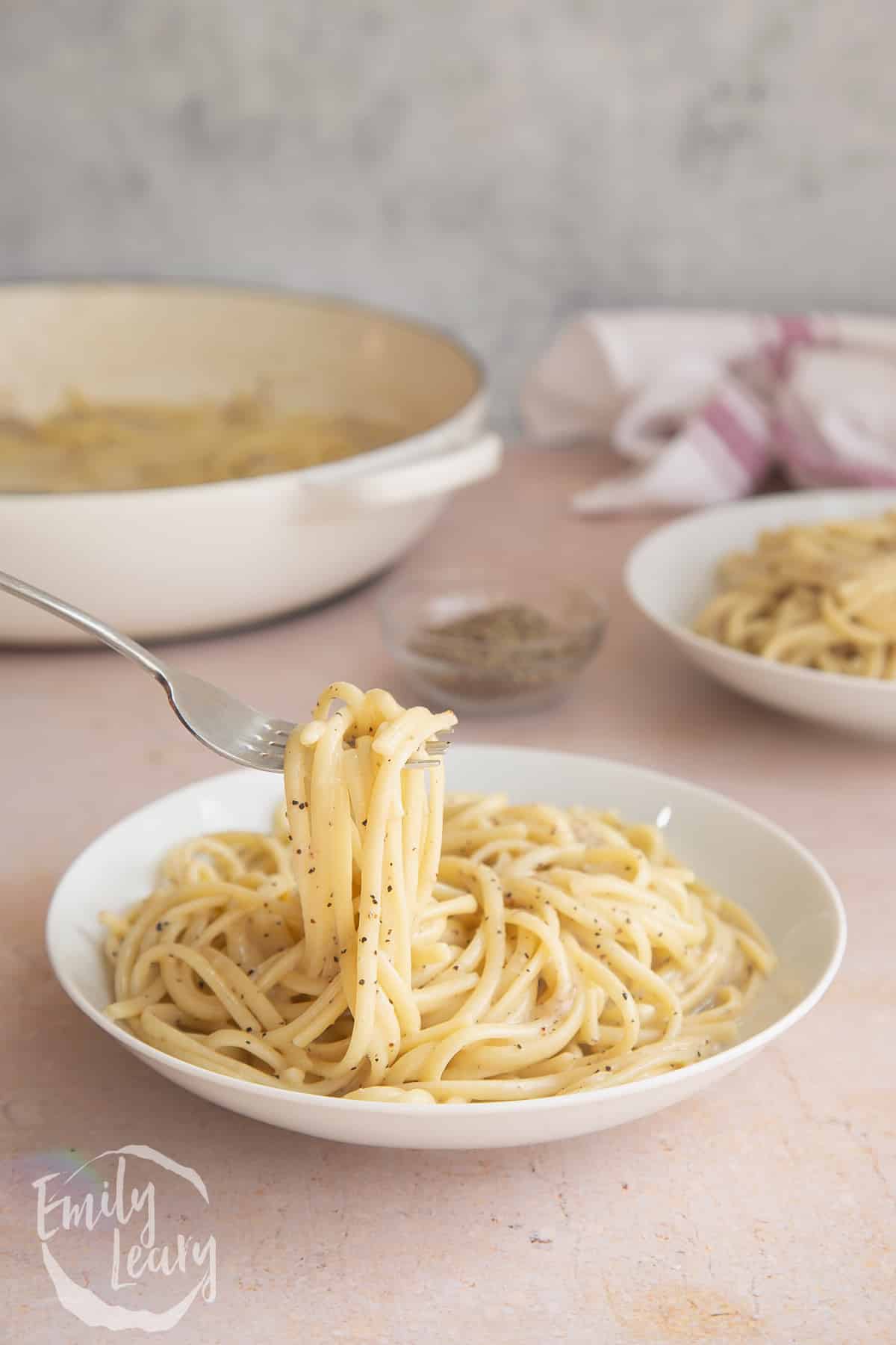 Linguine cacio e pepe in a white bowl with a fork spulling up a mouthful of pasta. 