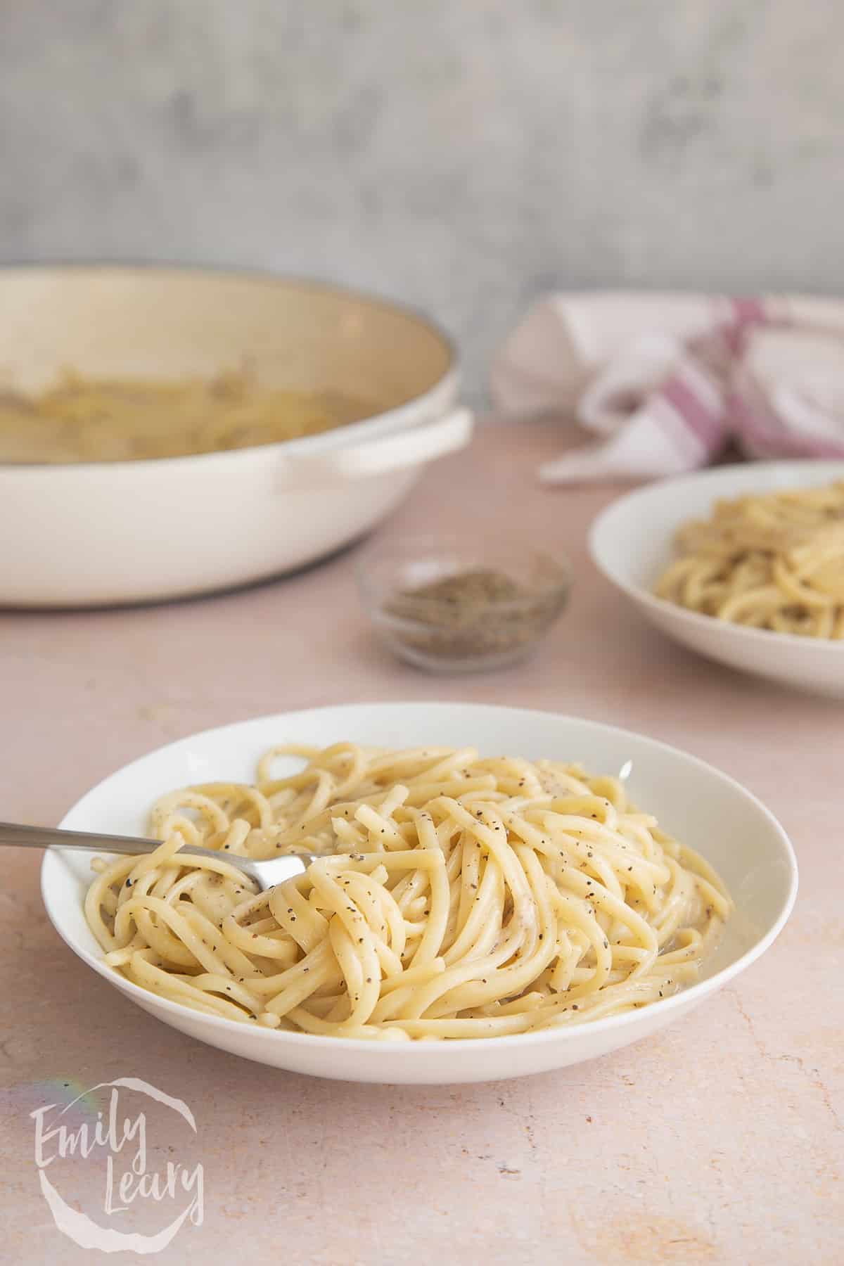 Linguine cacio e pepe in a white bowl with a fork stuck in the side. 