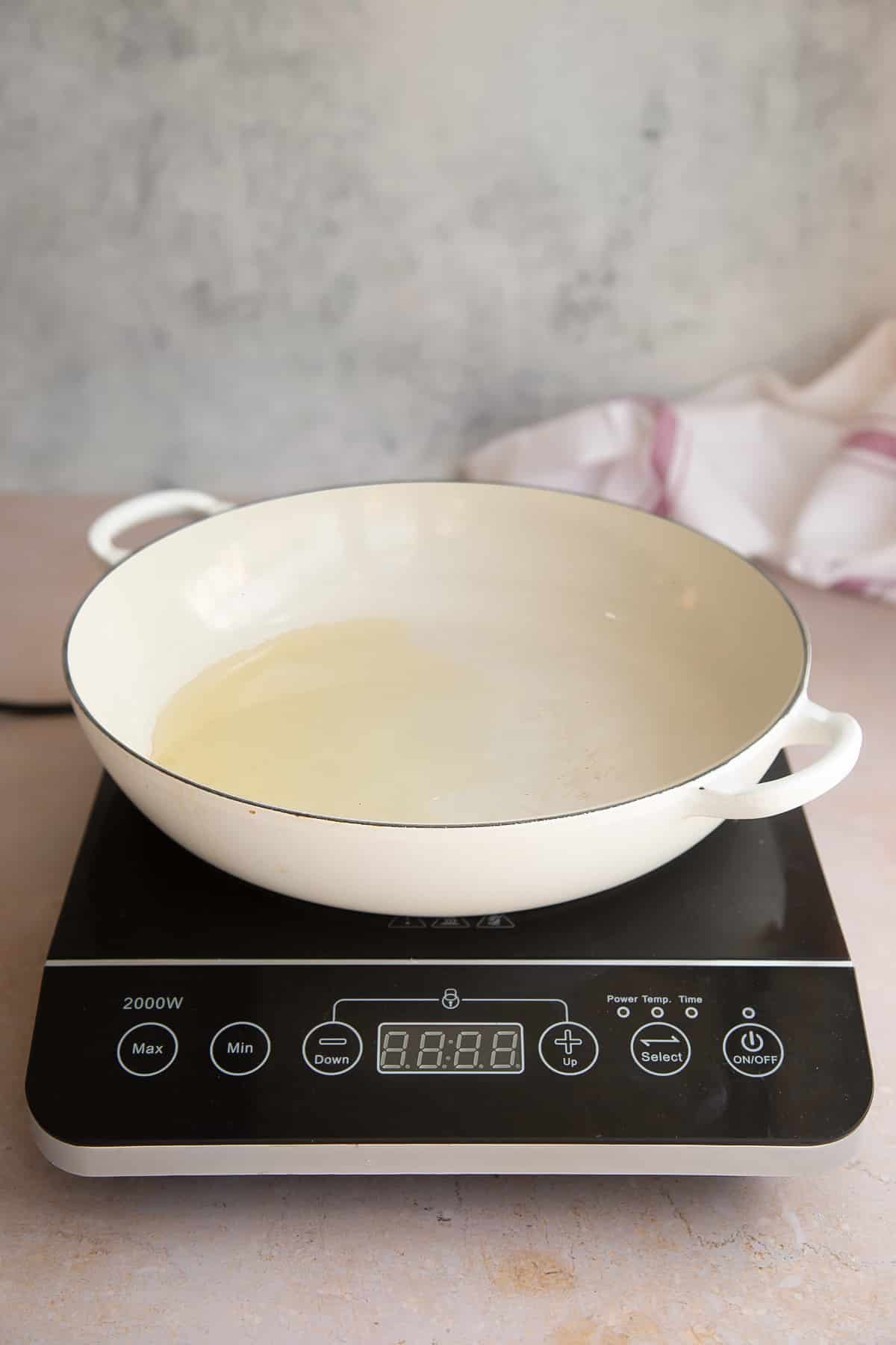 a white skillet pan on a induction hob heating oil.