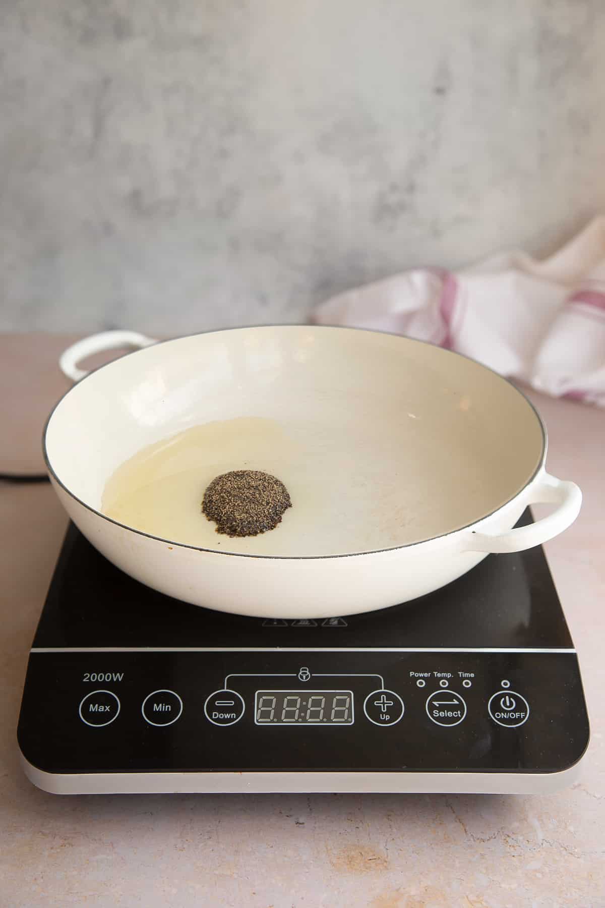 a white skillet with oil and pepper pan on a induction hob.