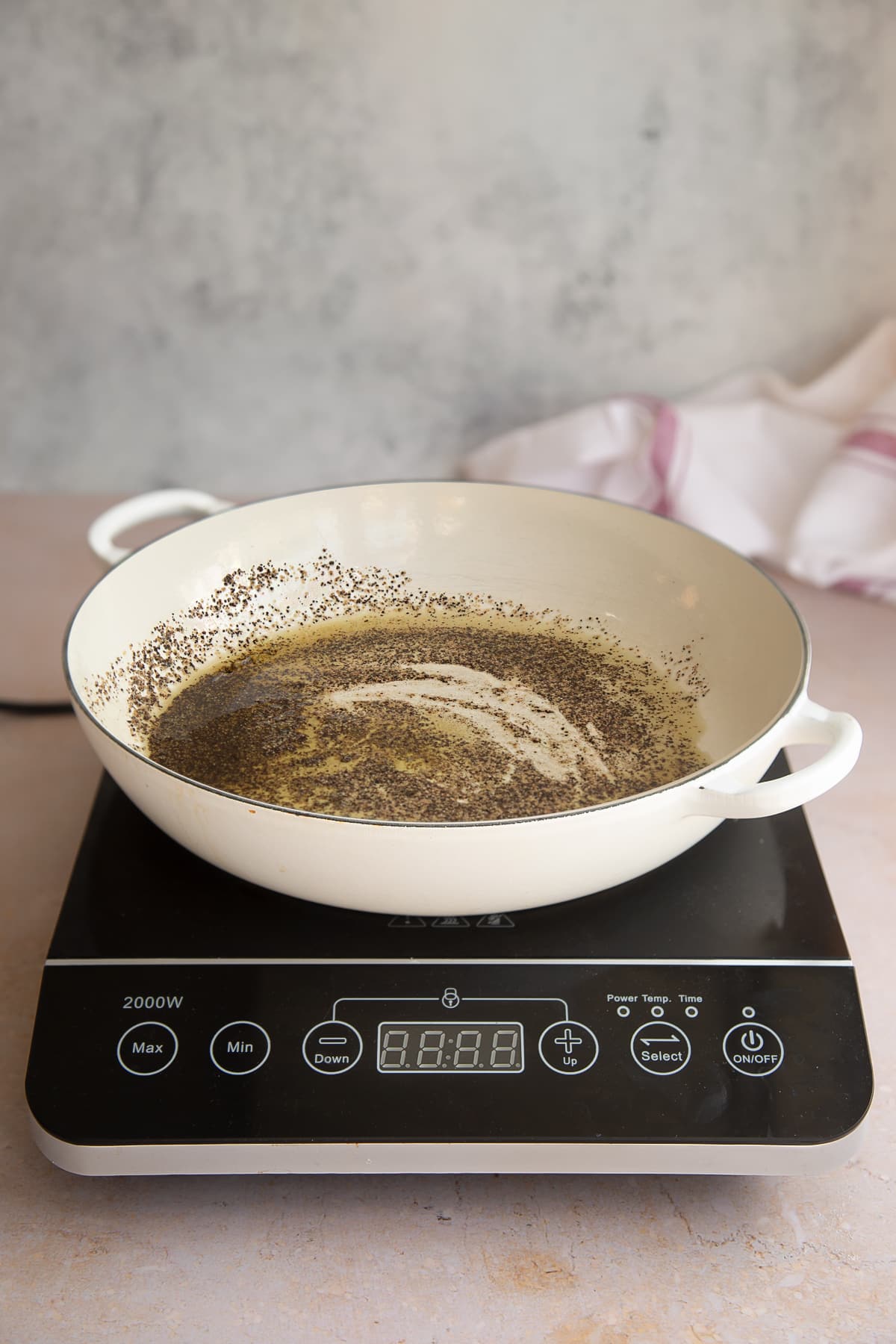 a white skillet with oil and pepper mixed together in a pan on a induction hob.