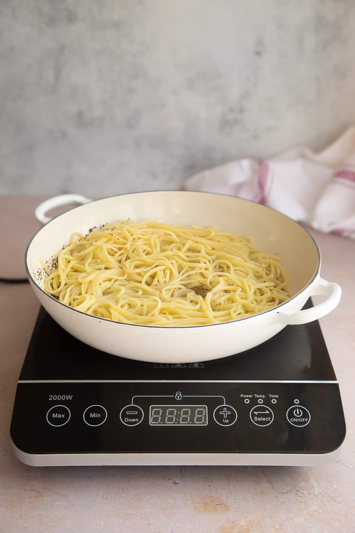 a white skillet pan with oil, pepper and cooked linguine in a on a induction hob.