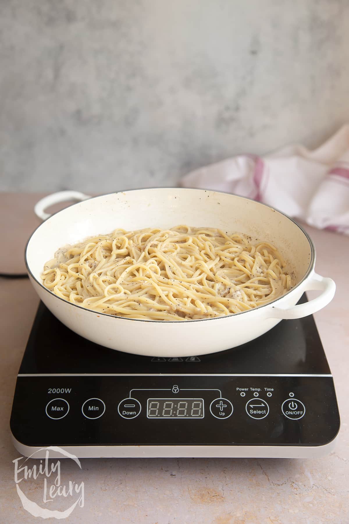 a white skillet pan with cooked linguine and cheese mixed together topped on a induction hob.