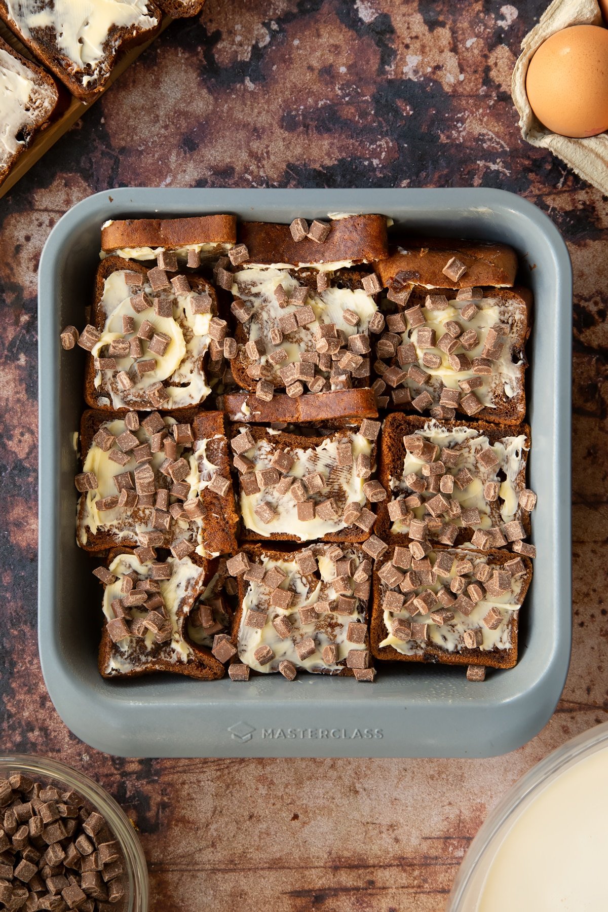 buttered malt loaf layers in a baking tin topped with chocolate chips.