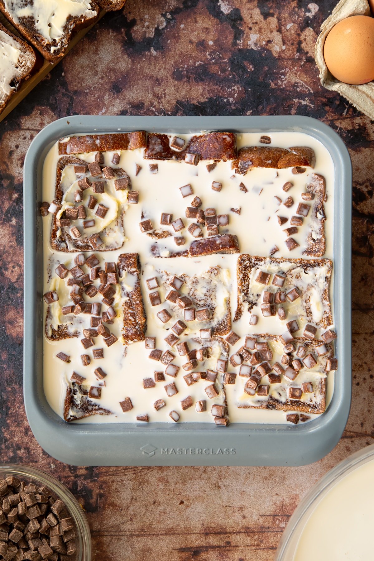 buttered malt loaf layers in a baking tin topped with chocolate chips and custard.