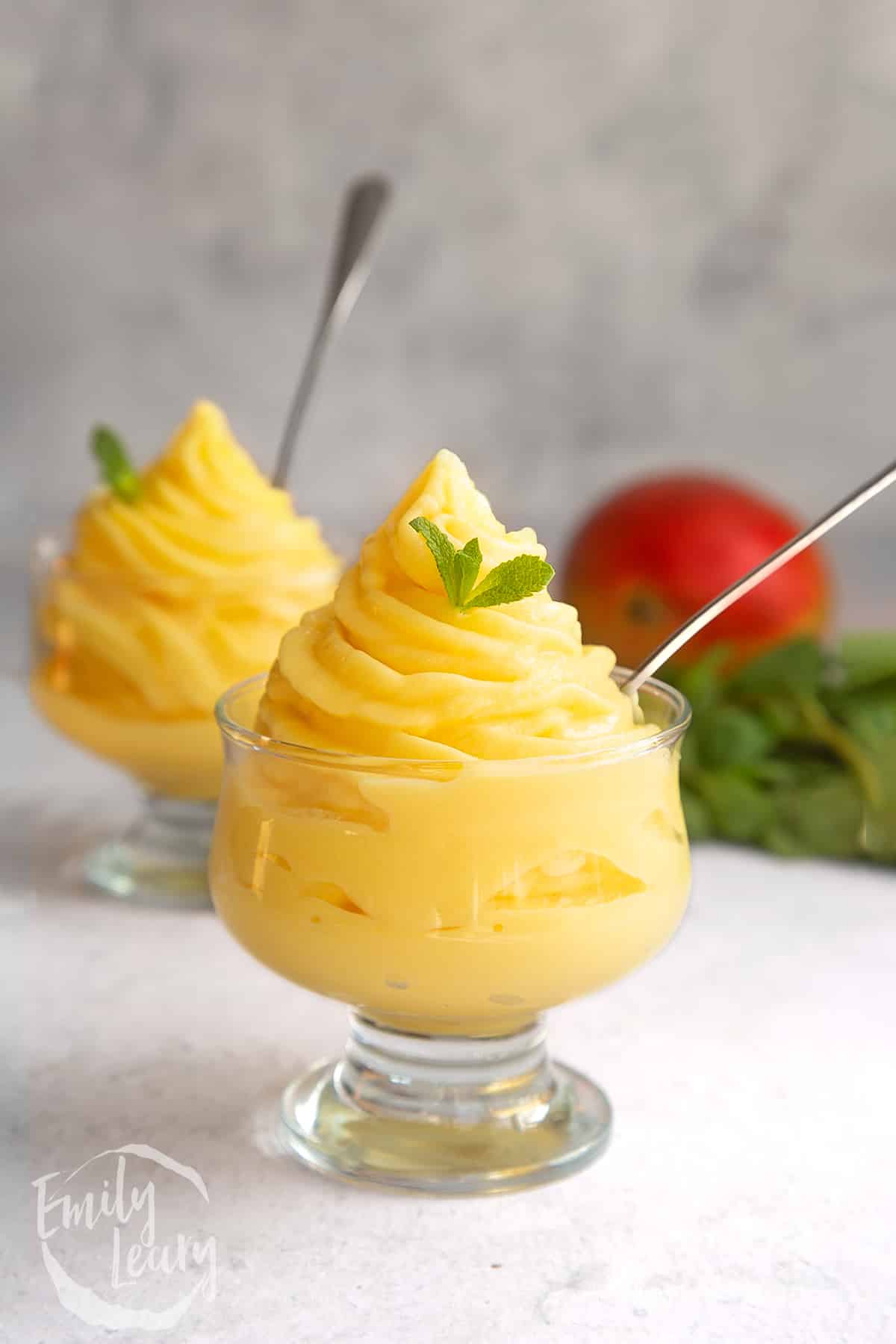 a decadent glass filled with mango ice cream with a spoon out the side and topped with a small mint leaf.