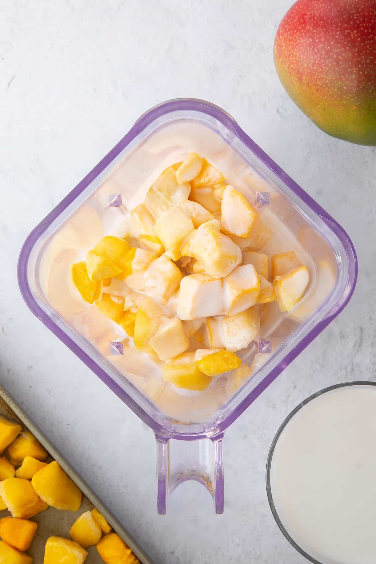 chunks of mango and coconut milk in a plastic blender cup.