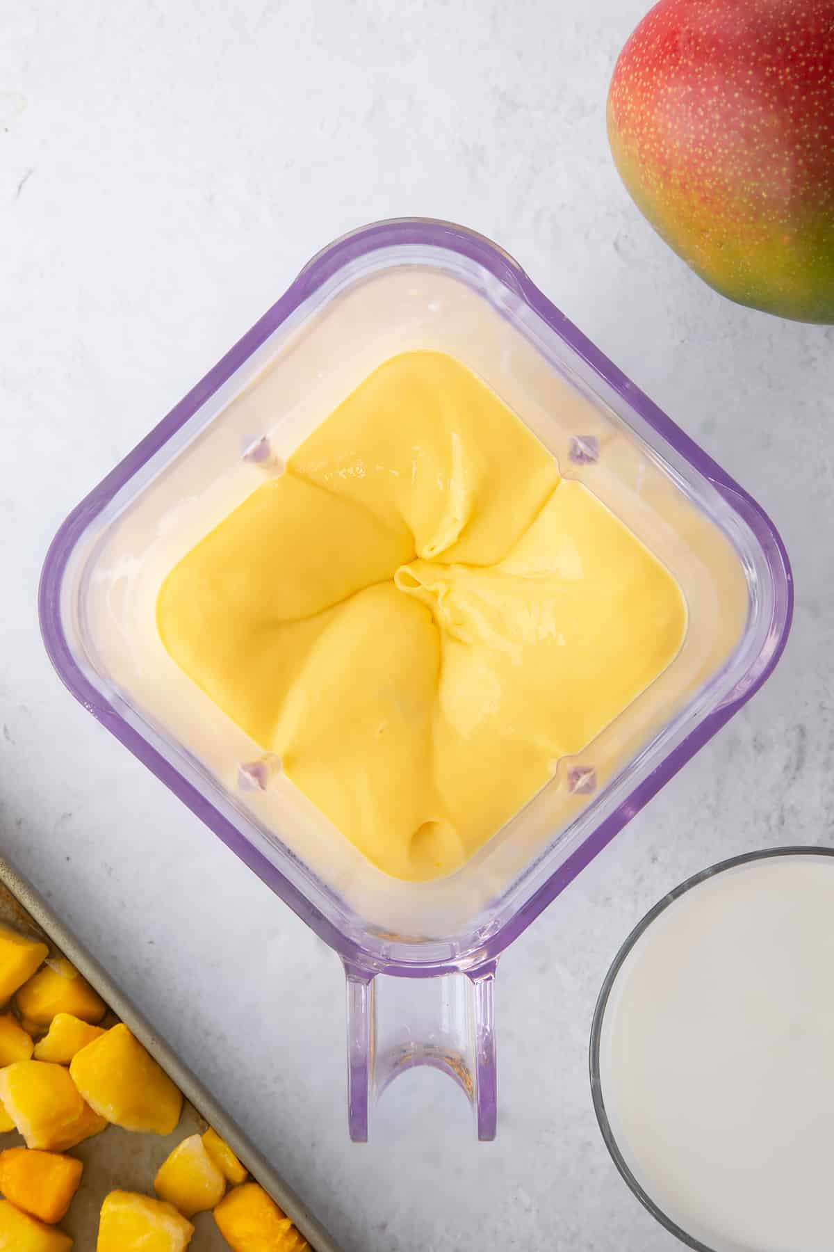 blended mango and coconut milk in a plastic belnder cup.