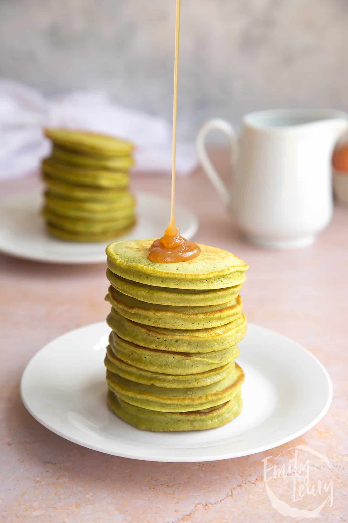 a stack of matcha pancakes on a white plate drizzled in syrup.