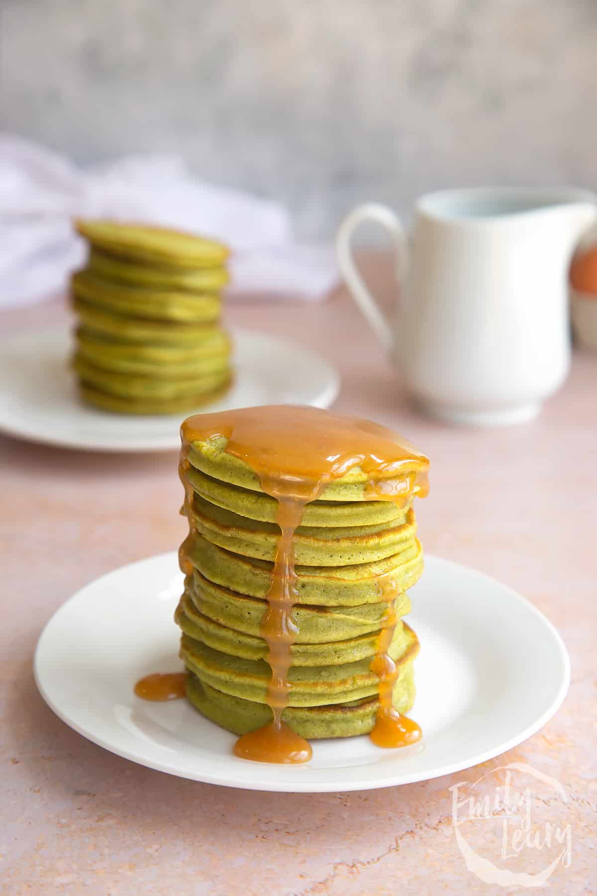 a stack of matcha pancakes on a white plate drizzled in syrup on a white plate.