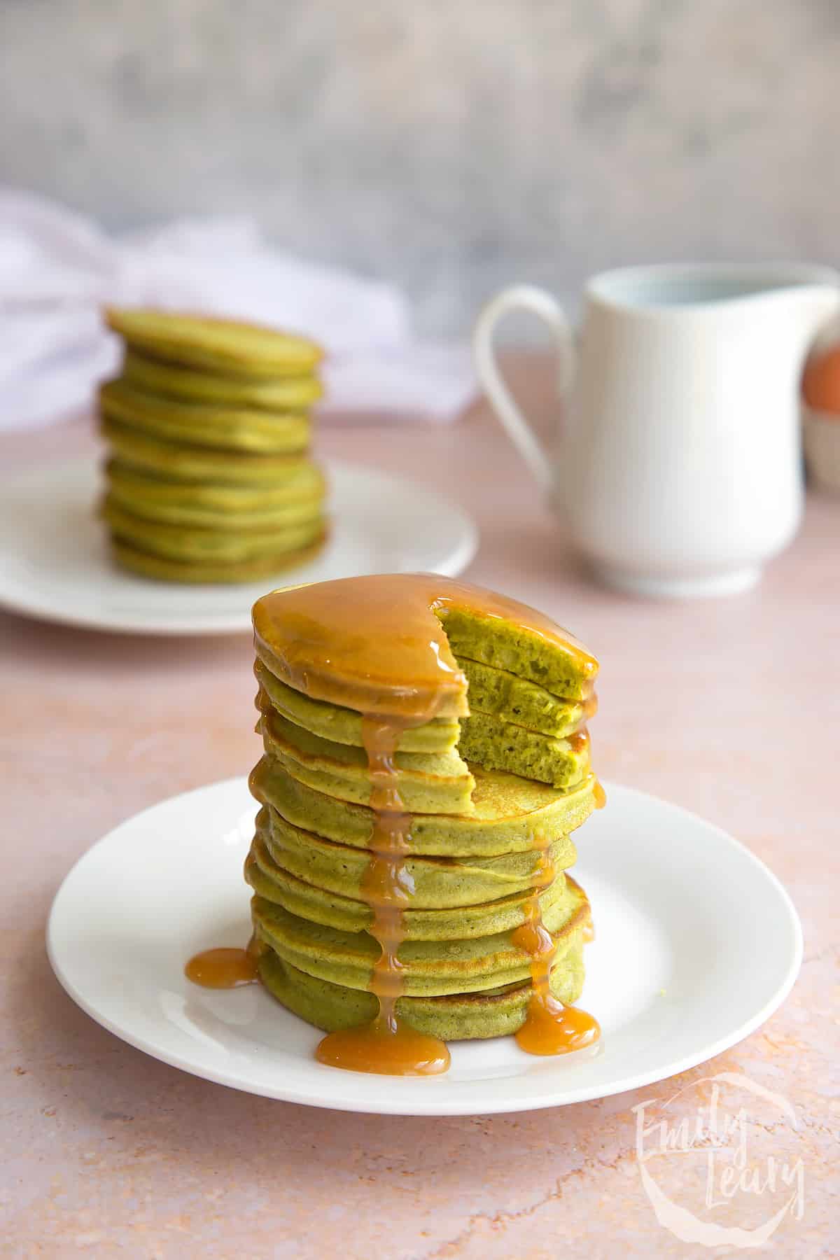 a stack of matcha pancakes covered in caramel sauce on a white plate with a bite taken from the top.