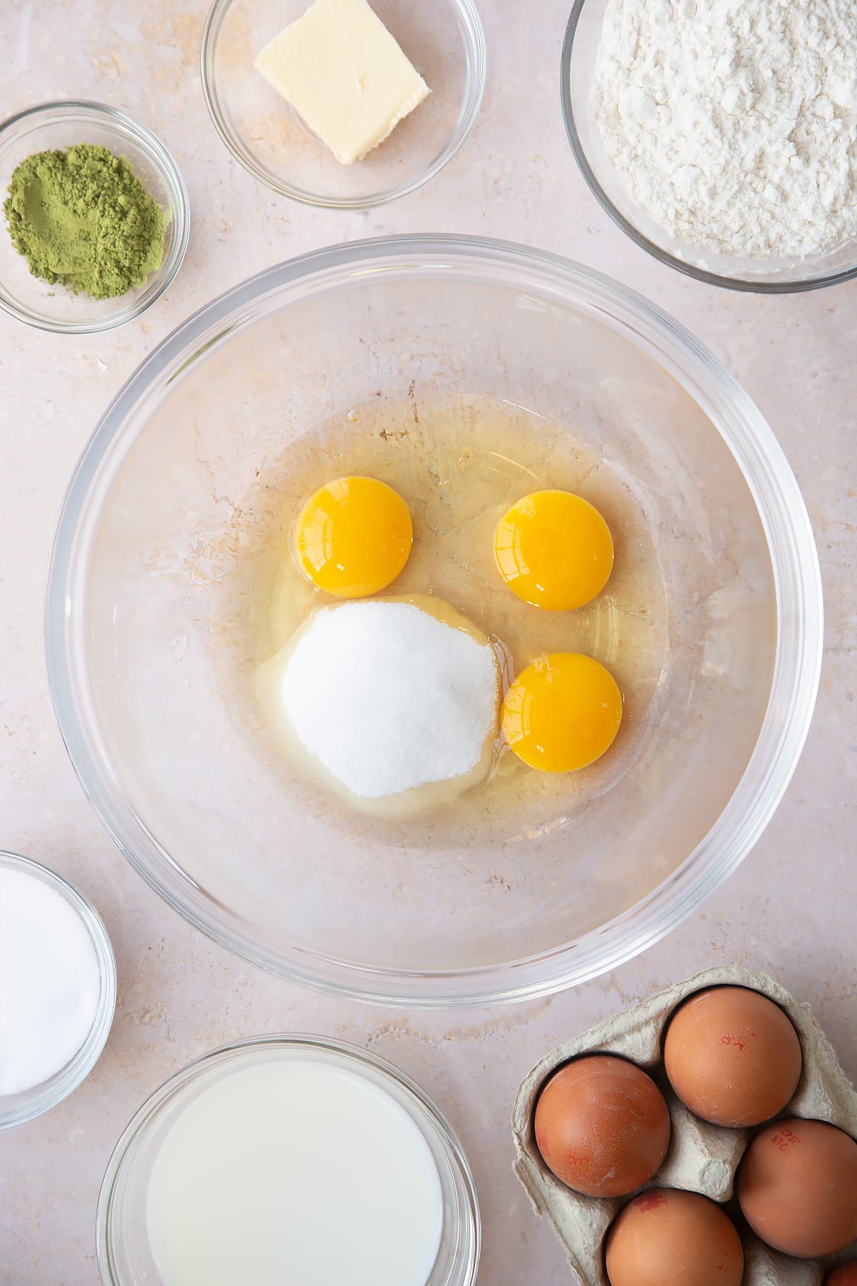 eggs and sugar in a large clear bowl surrounded by ingredients.
